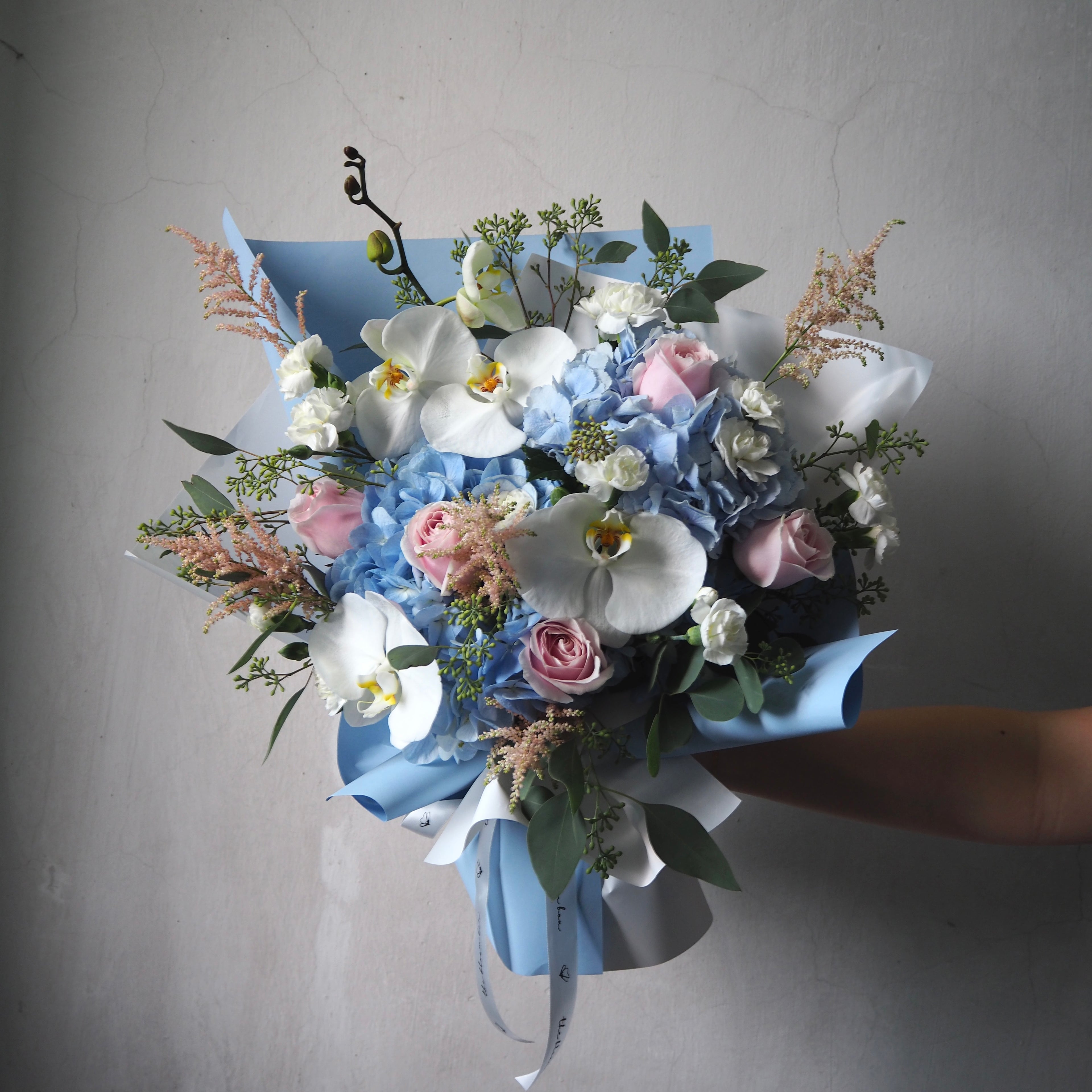 Bouquet of flowers with blue and pink tones held against a neutral background