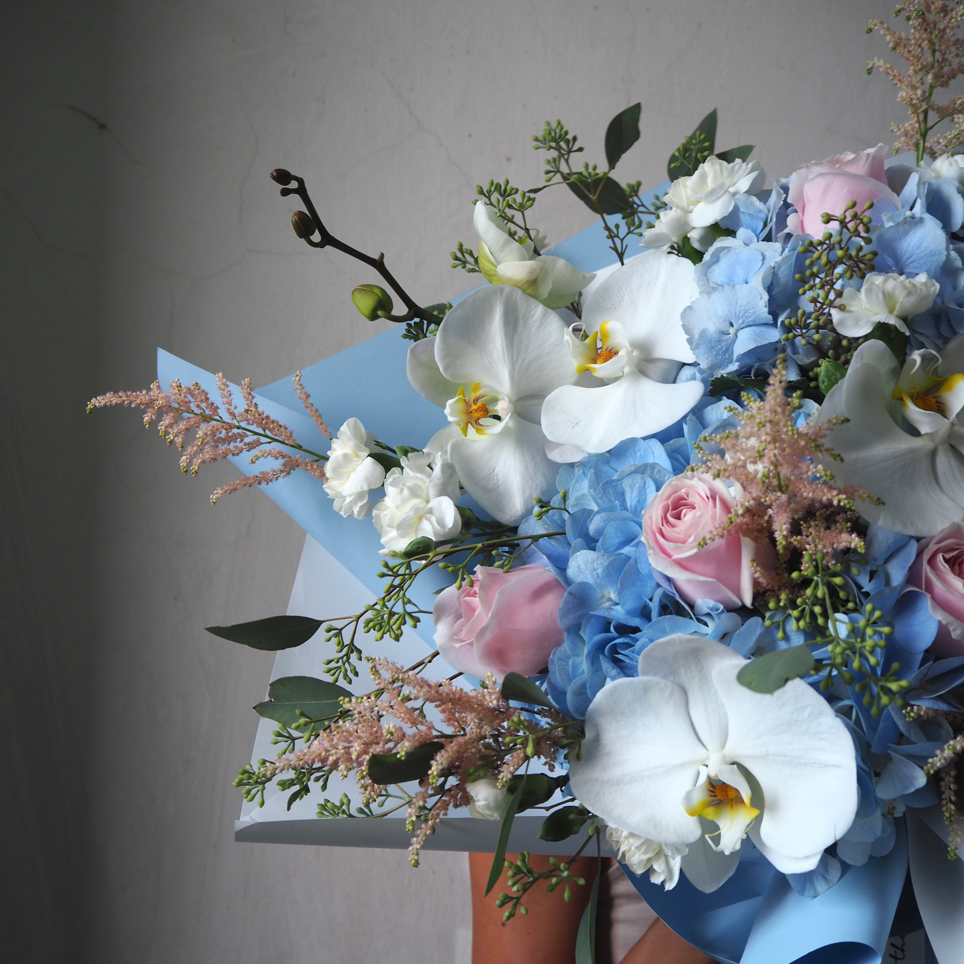 Bouquet of flowers with white orchids, blue hydrangeas, and pink roses on a gray background