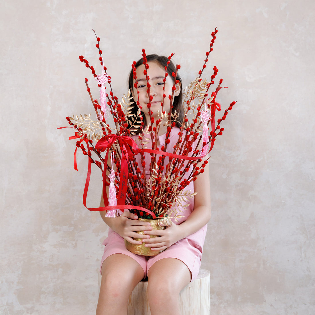 Person holding a bouquet of red and gold flowers against a plain background