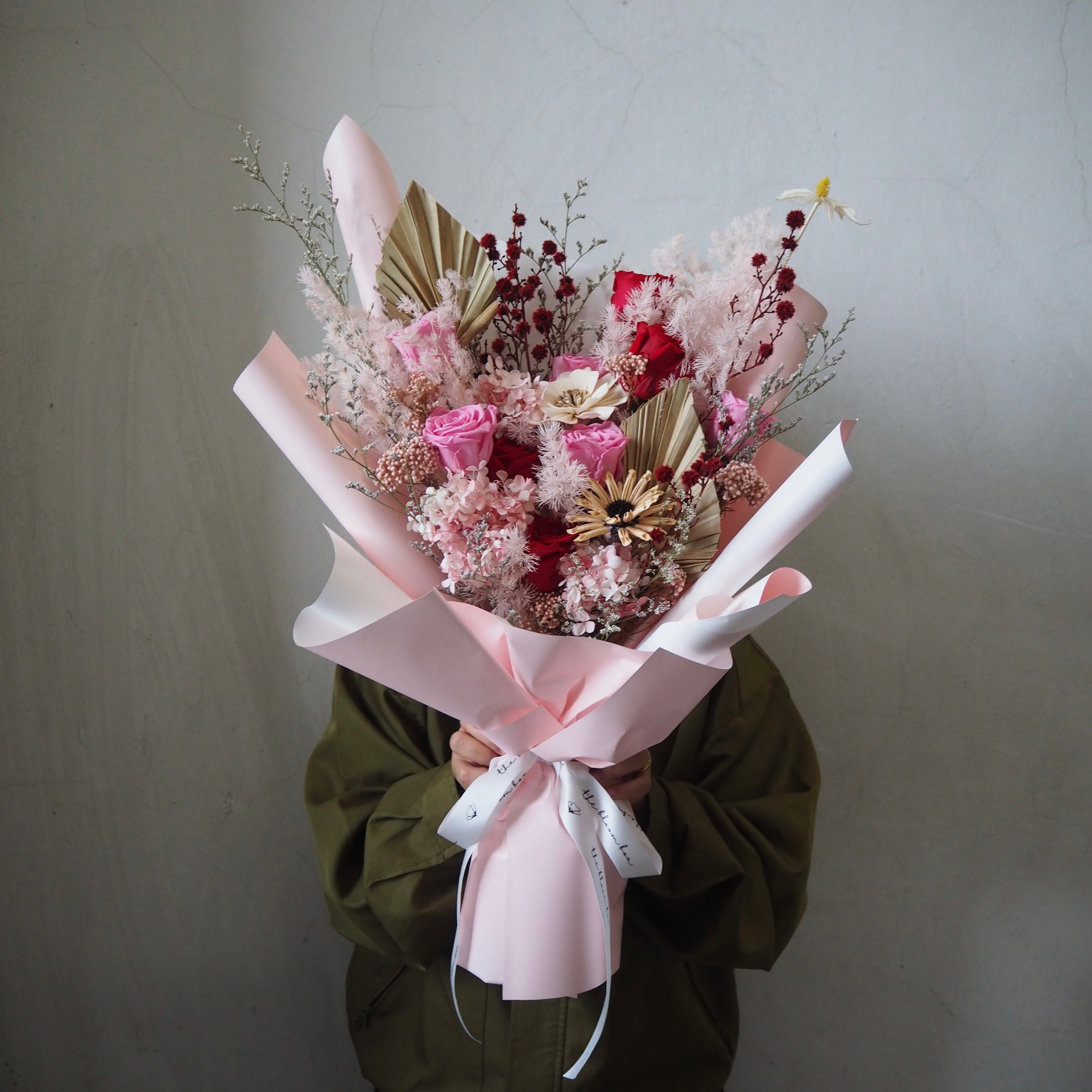 Bouquet of luxury preserved valentine flowers wrapped in pink paper held by a person