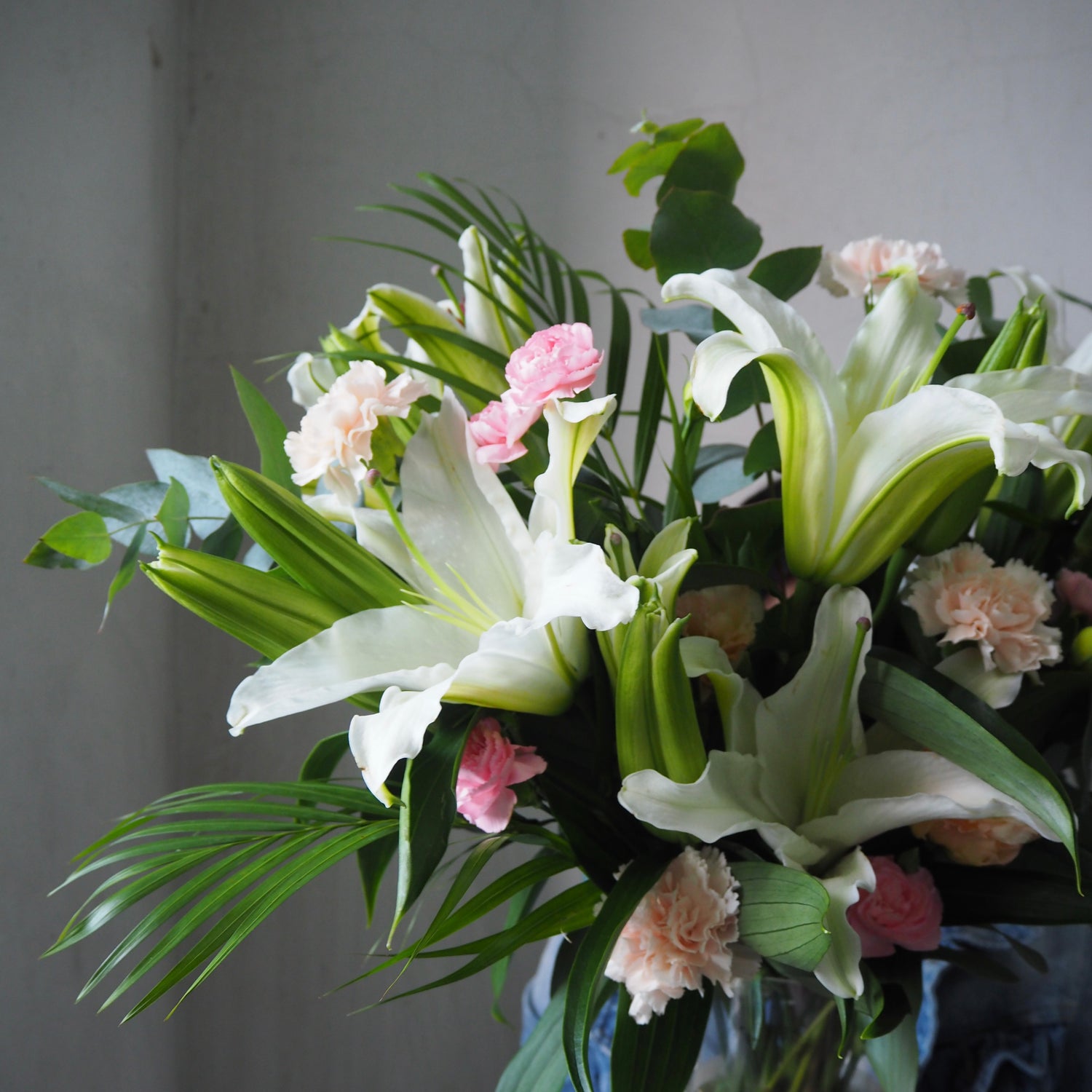 Bouquet of white lilies and pink flowers with green leaves in a vase against a gray background