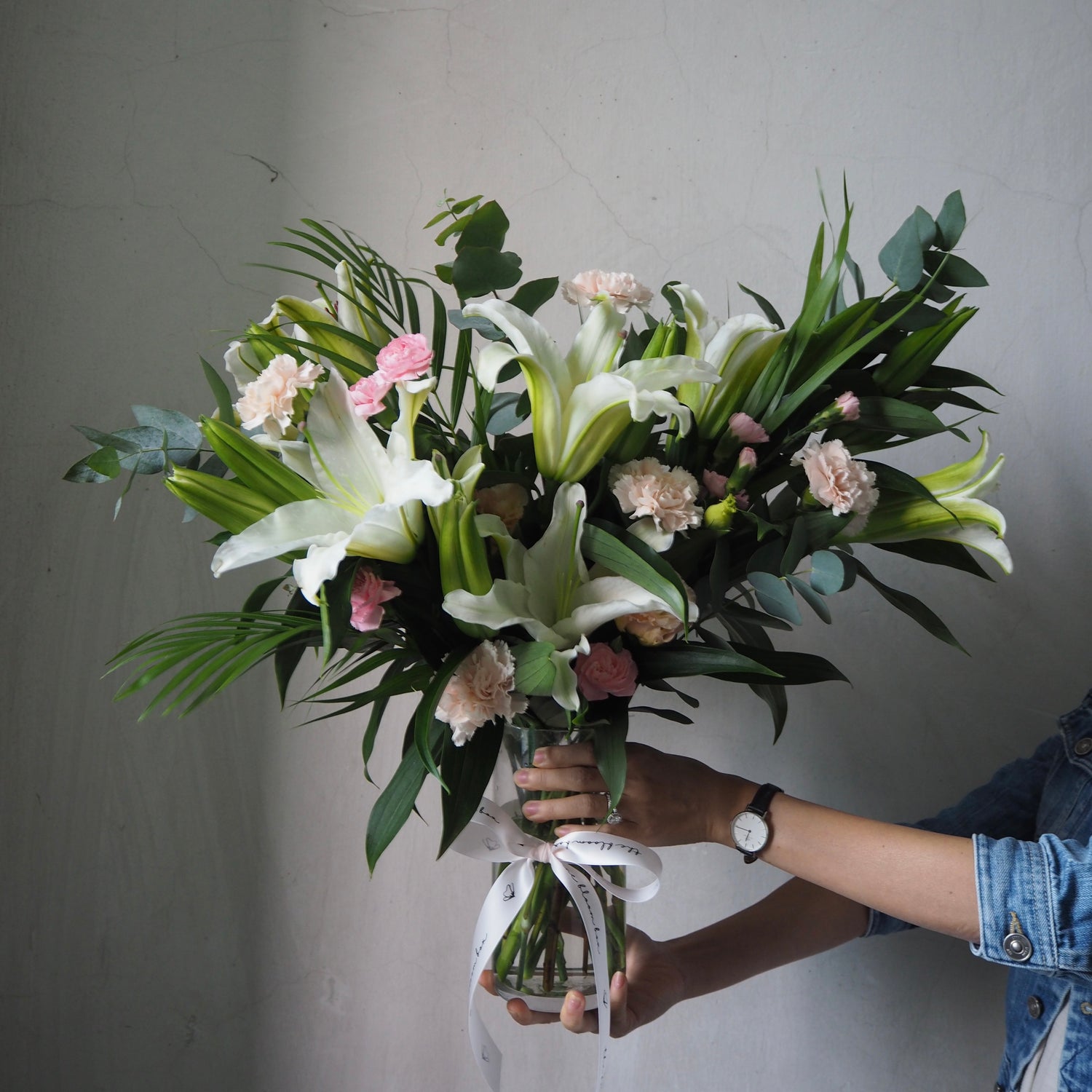 Bouquet of white lilies flowers held by a person against a plain background