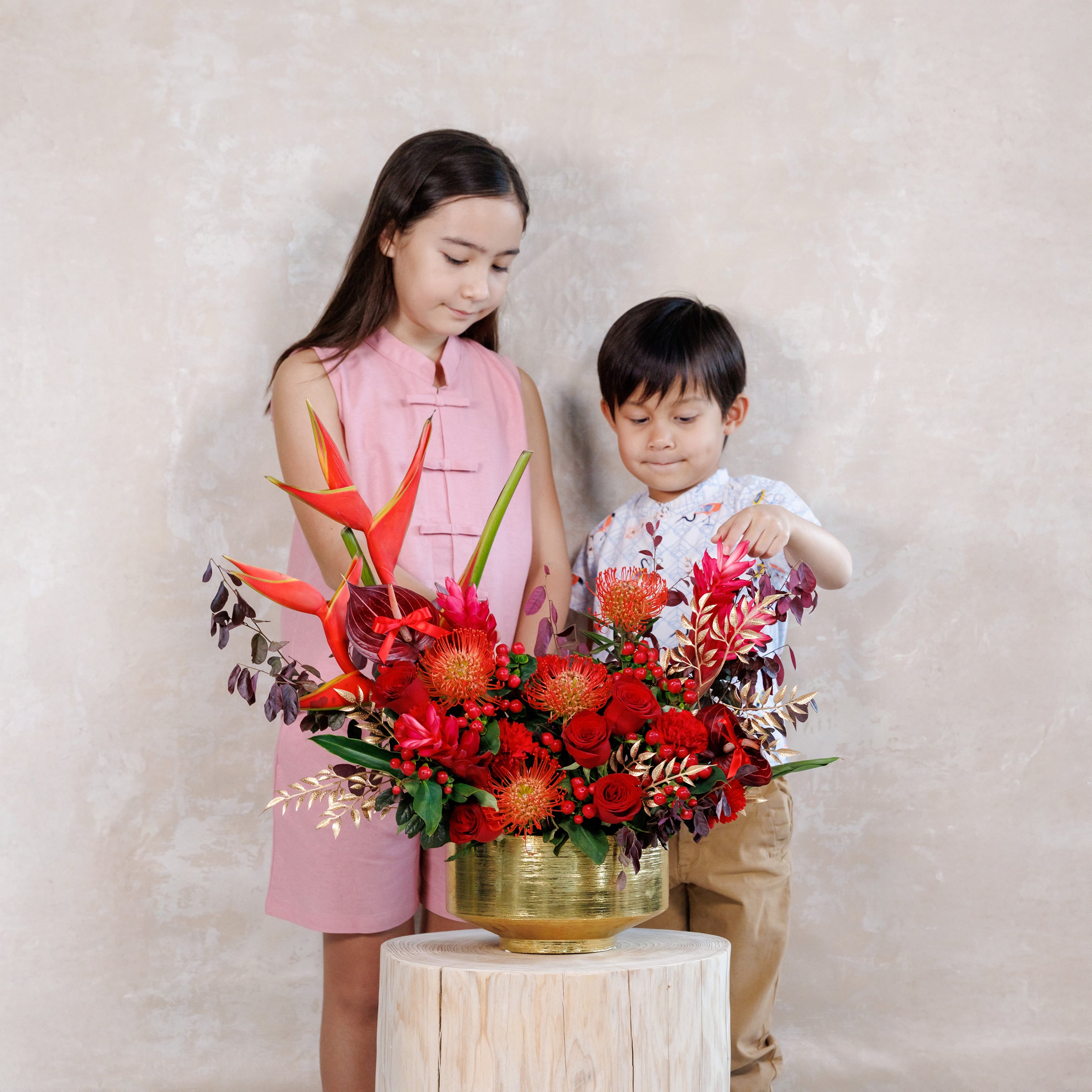 Two children with a large floral arrangement on a light background