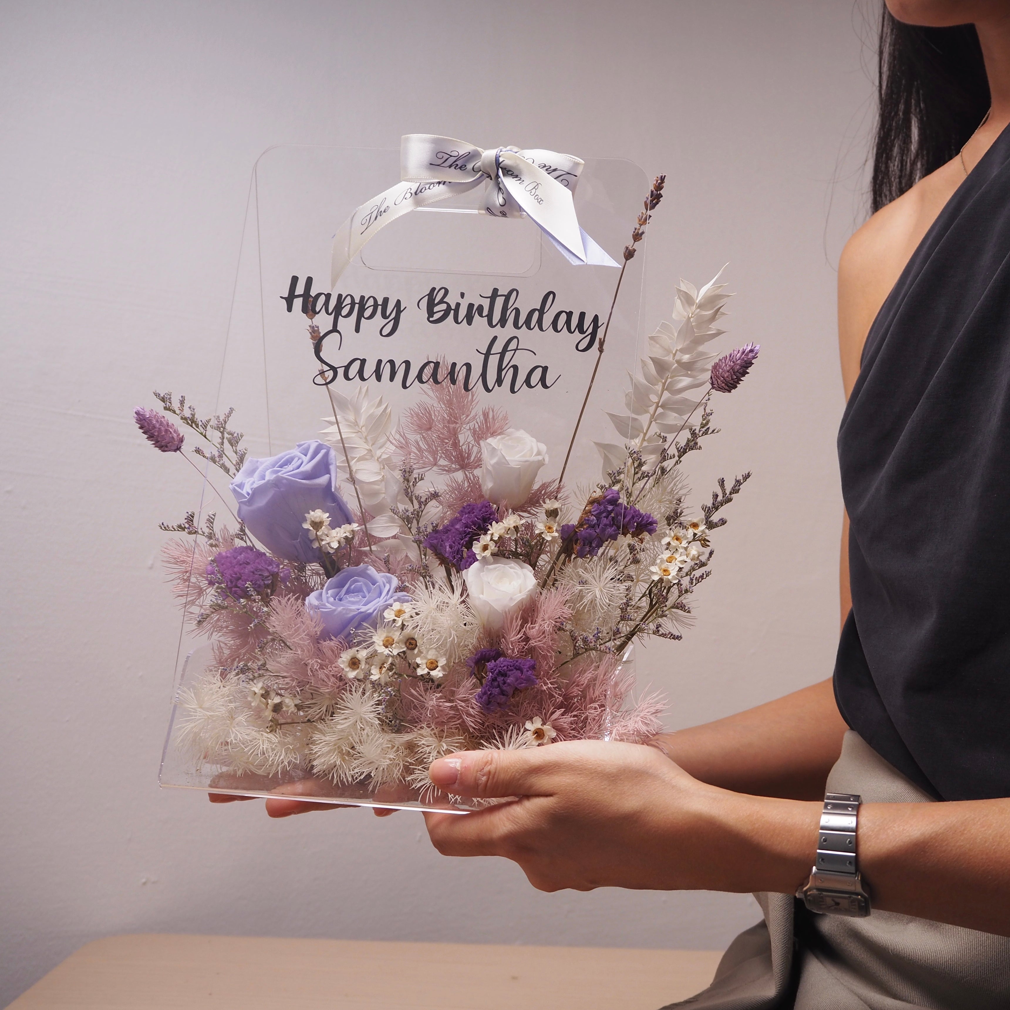 lady holding transparent flower box with purple preserved flowers