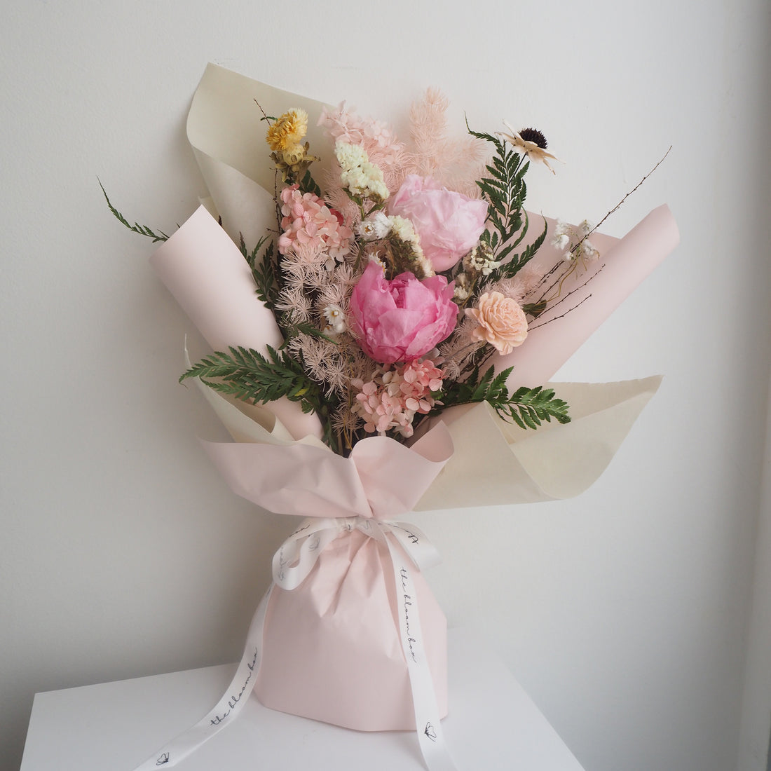 Bouquet of flowers wrapped in pink paper on a white surface with a light gray background