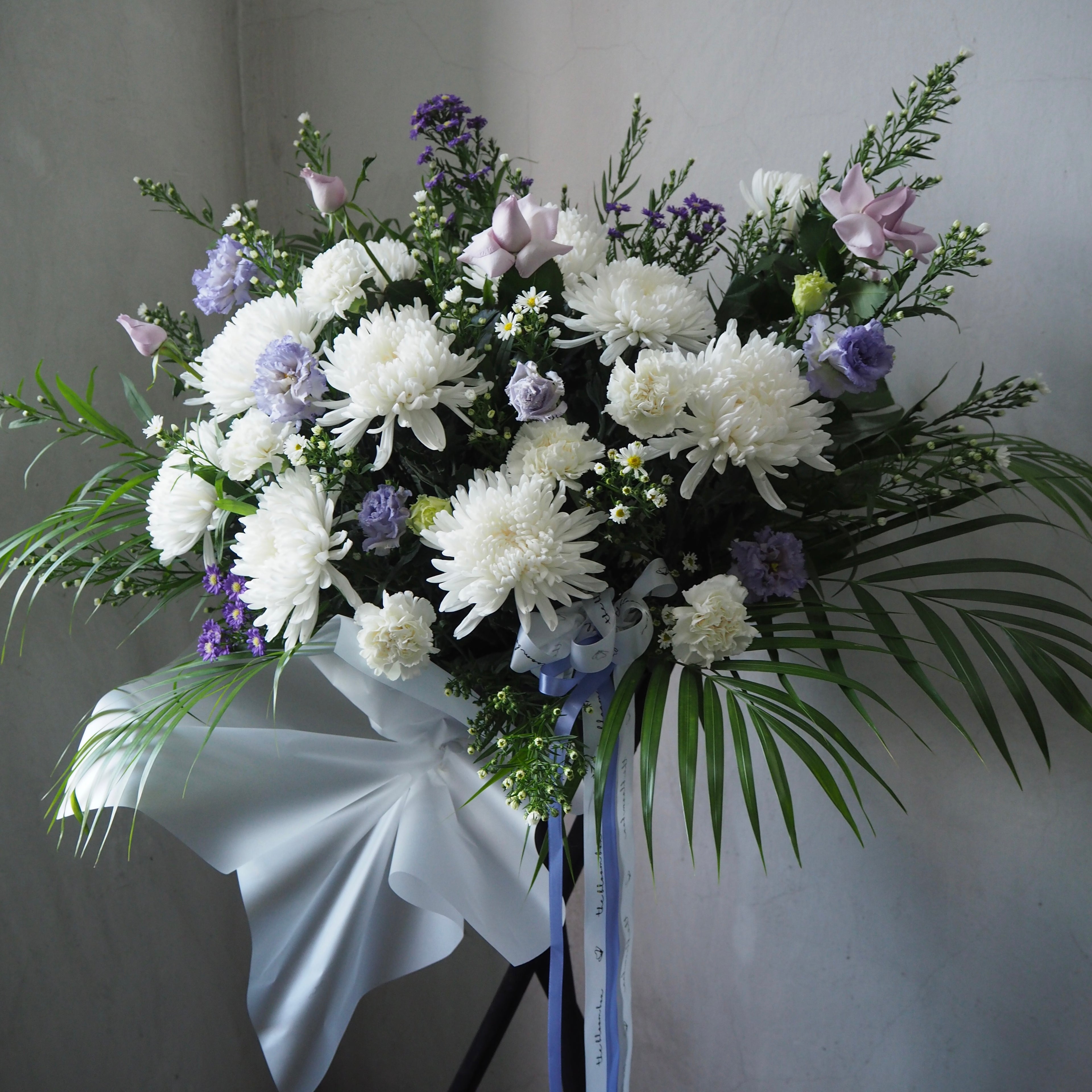 Bouquet of white and purple flowers with greenery on a stand against a plain background