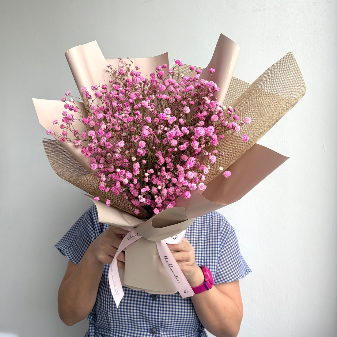 Bouquet of pink flowers wrapped in brown paper held by a person against a white background