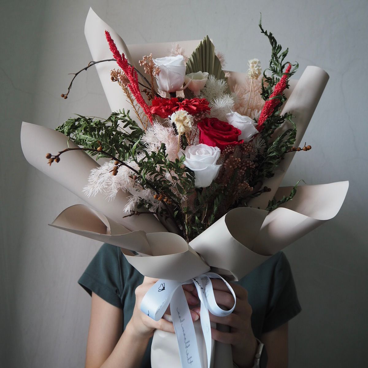 Bouquet of flowers wrapped in white paper held by a person against a plain background