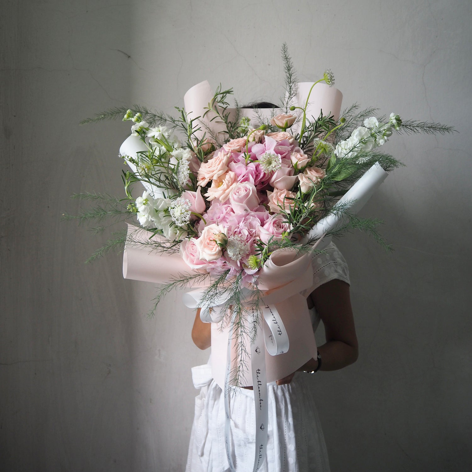 Person holding a bouquet of flowers in a pink box against a gray background