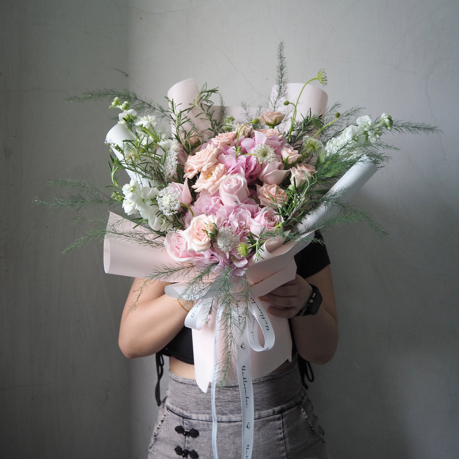 Person holding a bouquet of pink and white flowers against a plain background