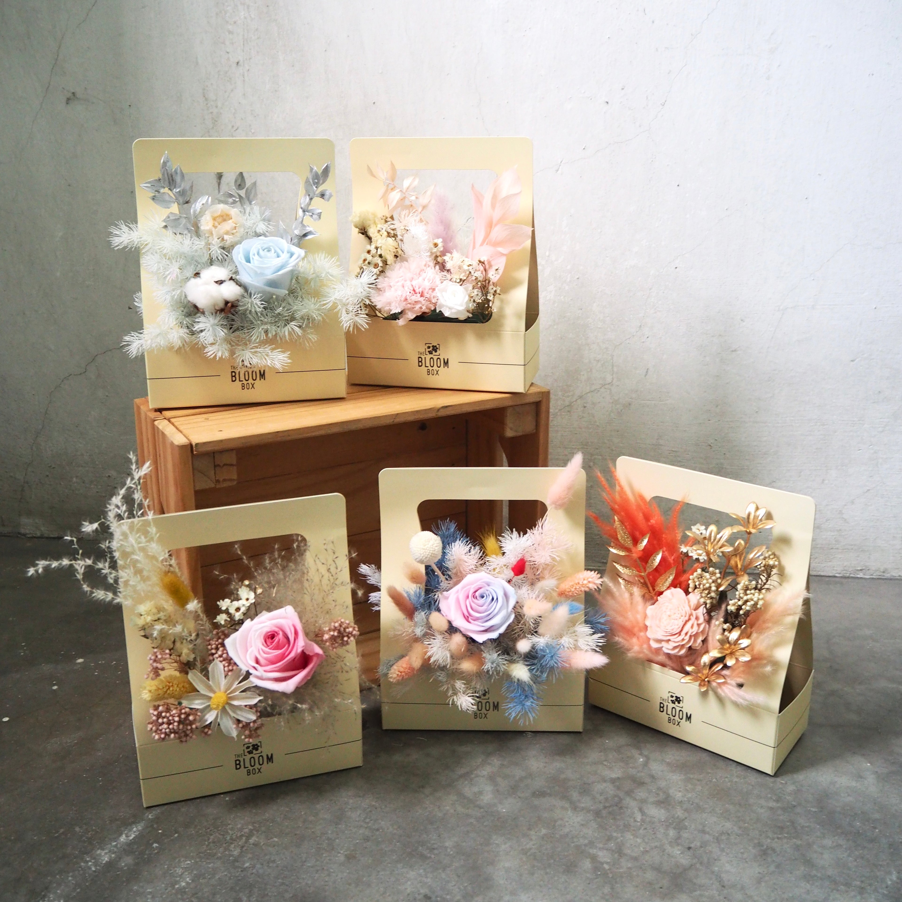Decorative flower arrangements in wooden boxes on a gray surface with a neutral background.