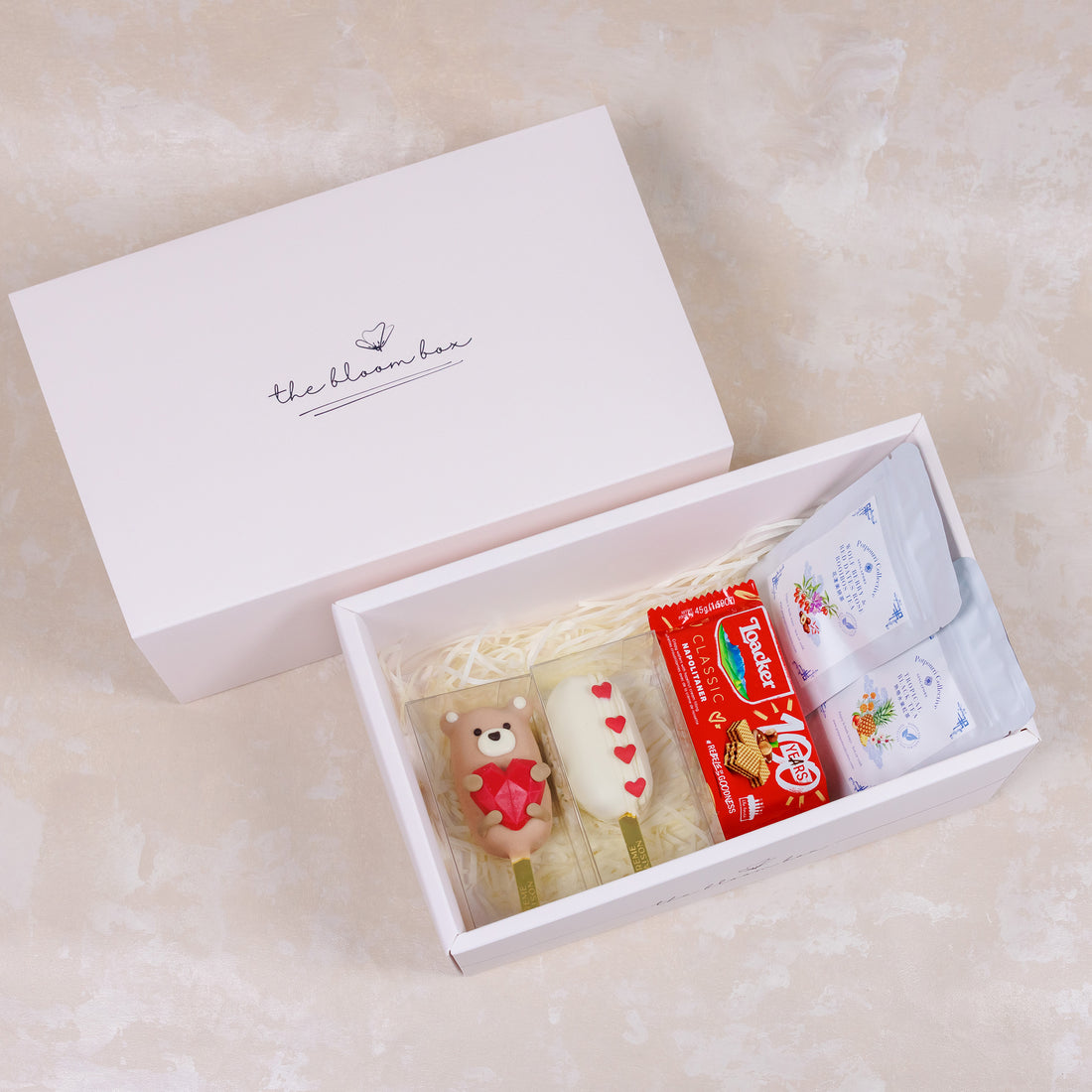 Gift box with a teddy bear, cake, and tea bags on a light background