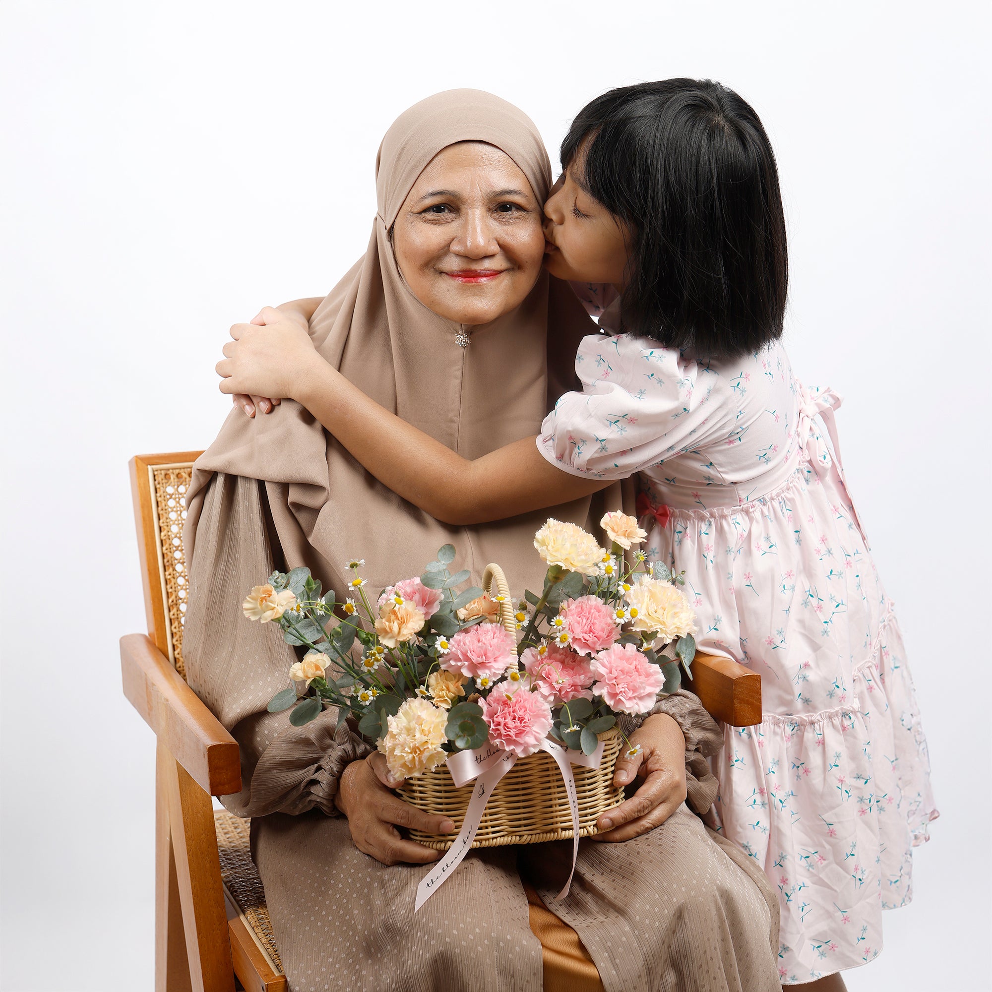 Woman in hijab holding flowers, embraced by a child on a white background
