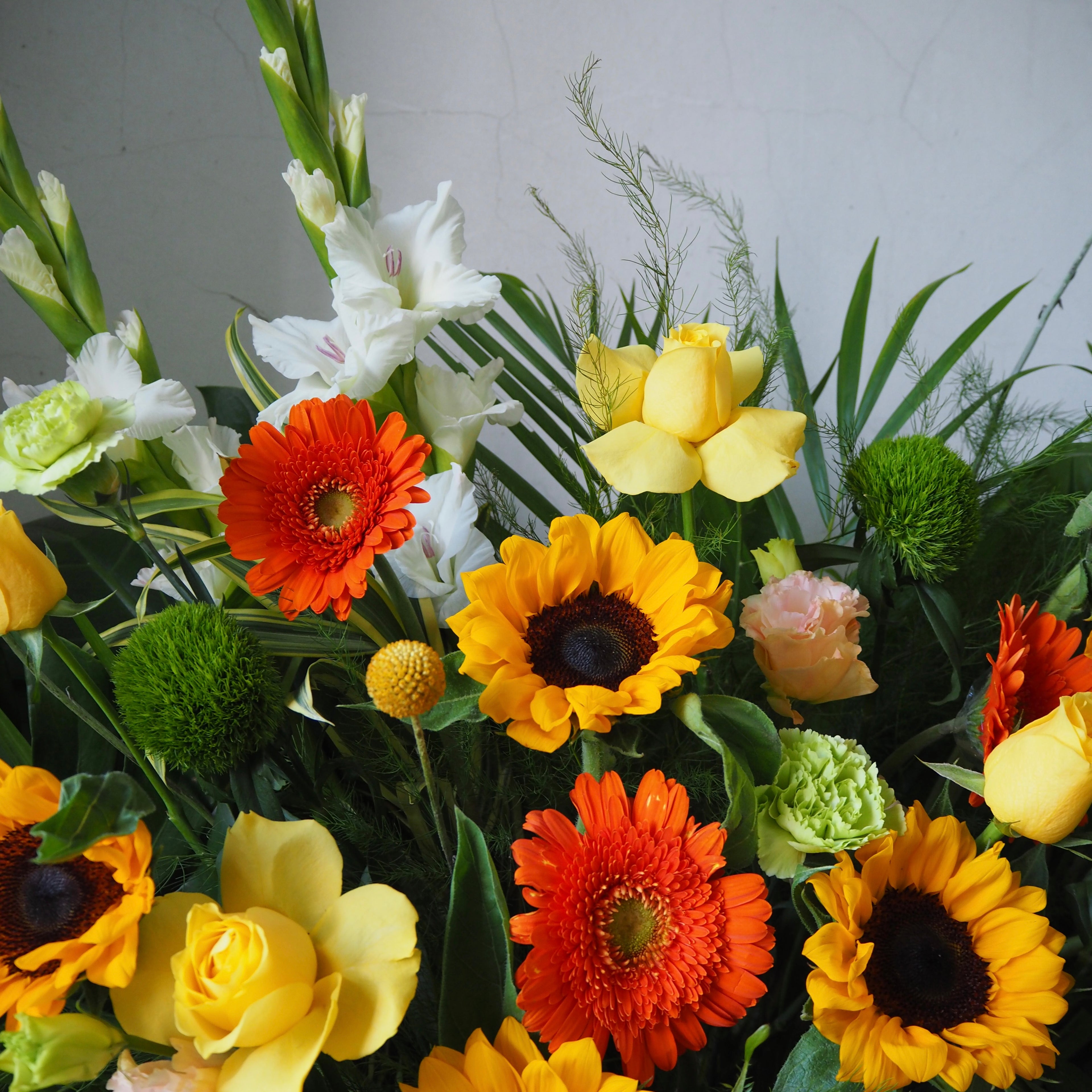 Bouquet of colorful flowers including sunflowers, daisies, and greenery on a neutral background.