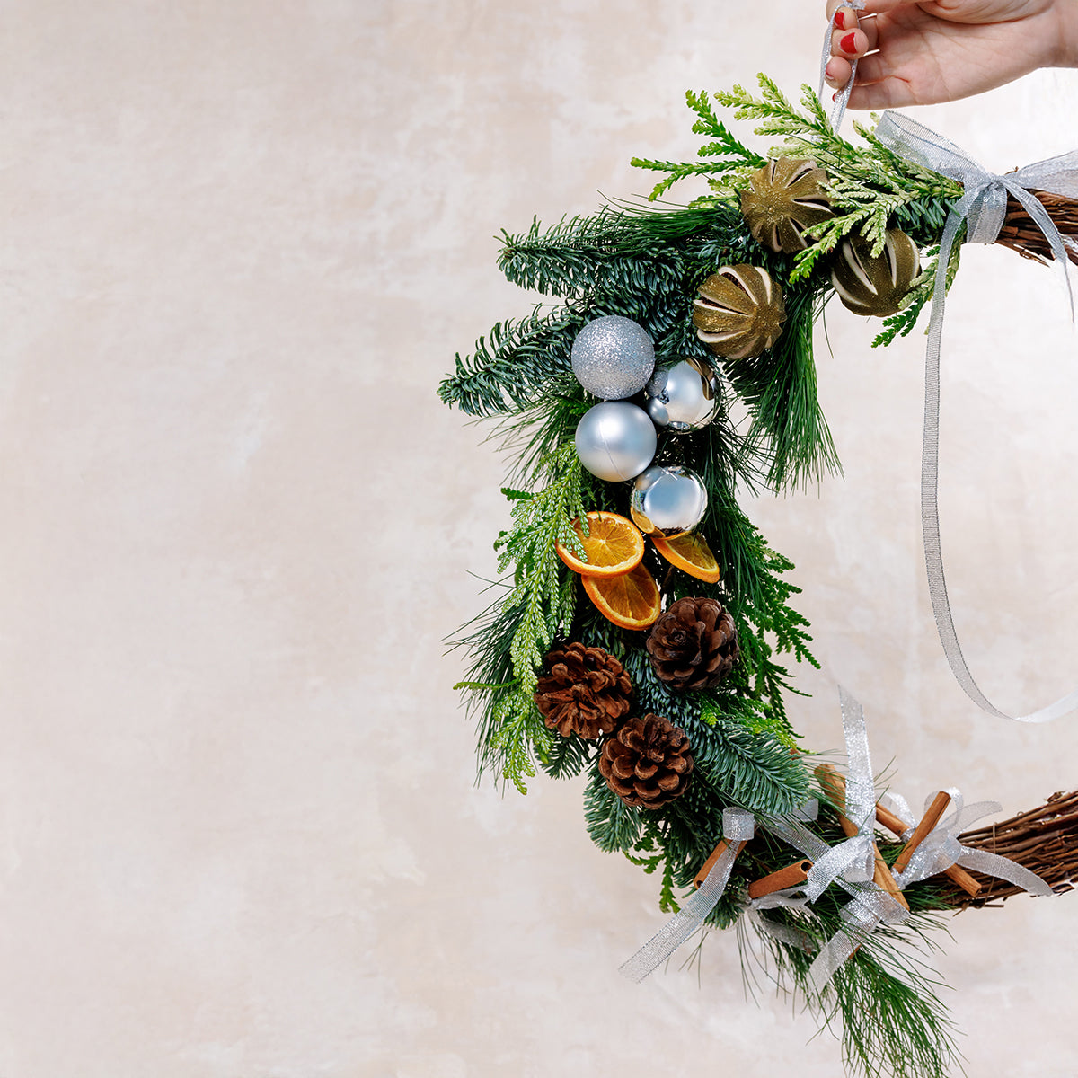 Decorative wreath with greenery, ornaments, and cinnamon sticks on a neutral background