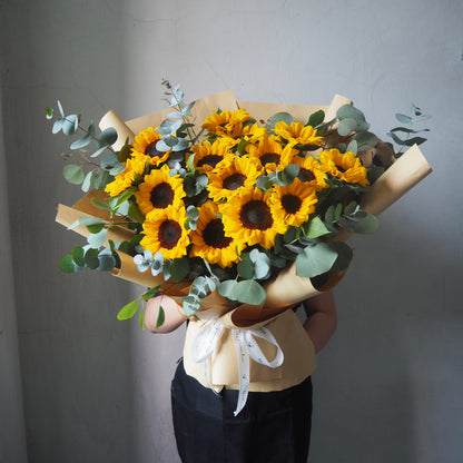 Bouquet of yellow sunflowers with green leaves held by a person against a gray background