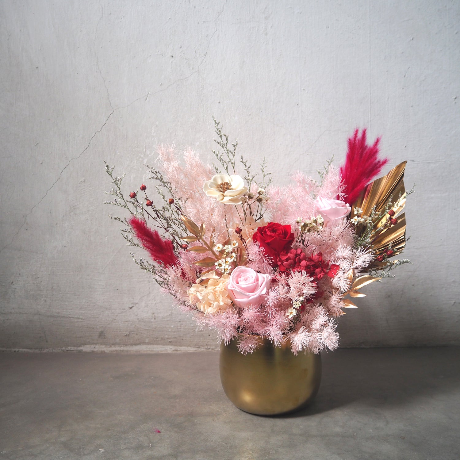 front view of premium preserved flower arrangement with red-pink flowers housed in gold vase