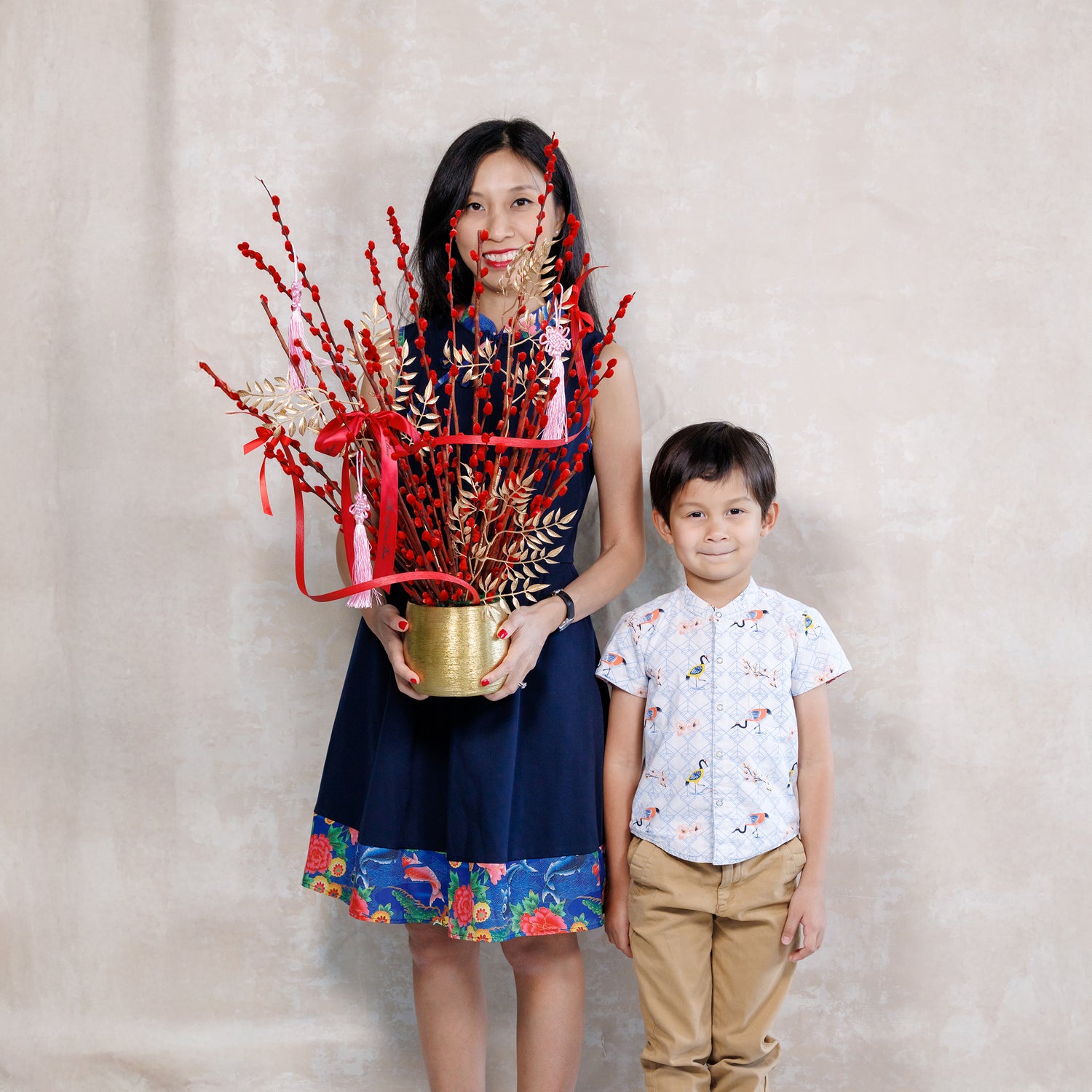Woman holding a decorative plant with red elements and a child standing next to her against a plain background