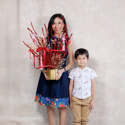 Woman holding a decorative plant with red elements and a child standing next to her against a plain background