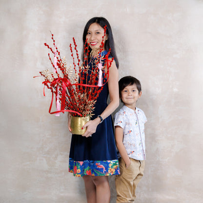 Woman holding a decorative plant with red ribbons and a child standing next to her against a plain background