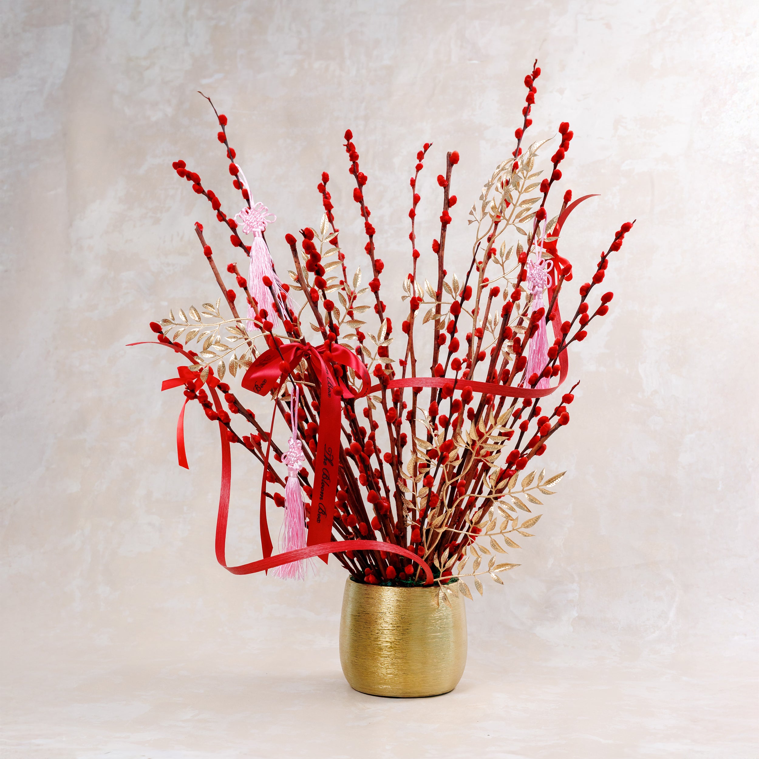 Bouquet of red and gold decorative sticks in a gold vase on a light background