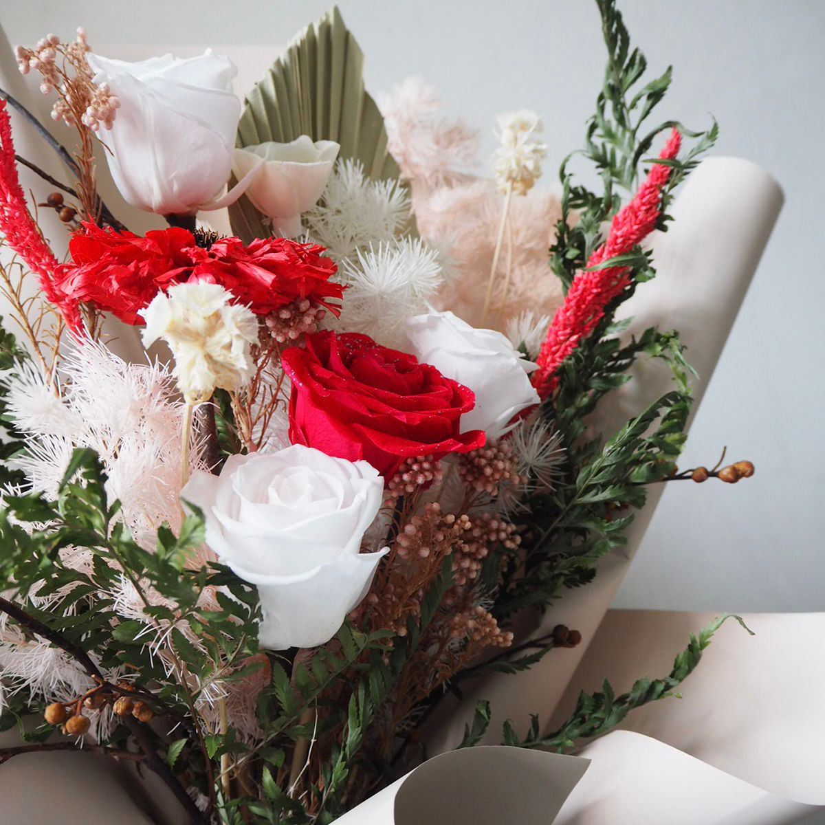 Bouquet of red, white, and pink flowers with green leaves on a light gray background