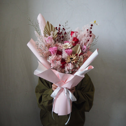 Bouquet of luxury preserved valentine flowers wrapped in pink paper held by a person
