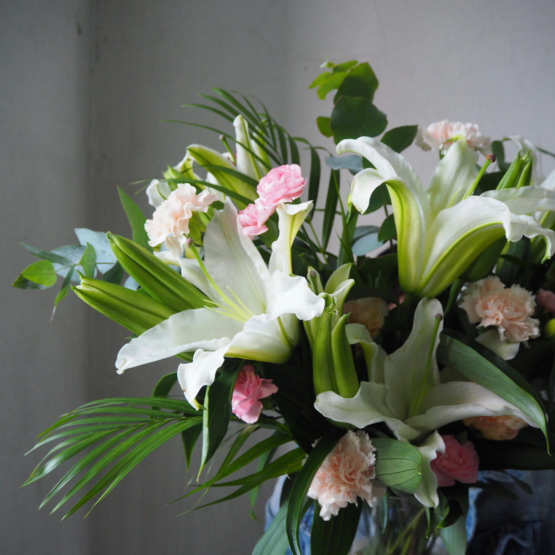 Bouquet of white lilies and pink flowers with green leaves in a vase against a gray background