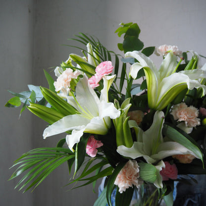 Bouquet of white lilies and pink flowers with green leaves in a vase against a gray background