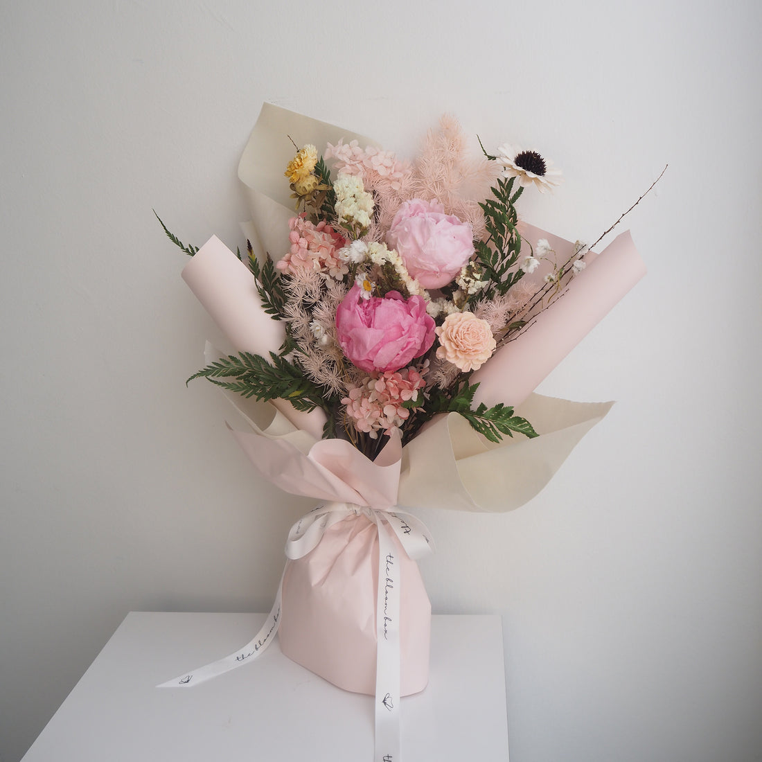 Bouquet of flowers wrapped in pink paper on a white surface with a light gray background