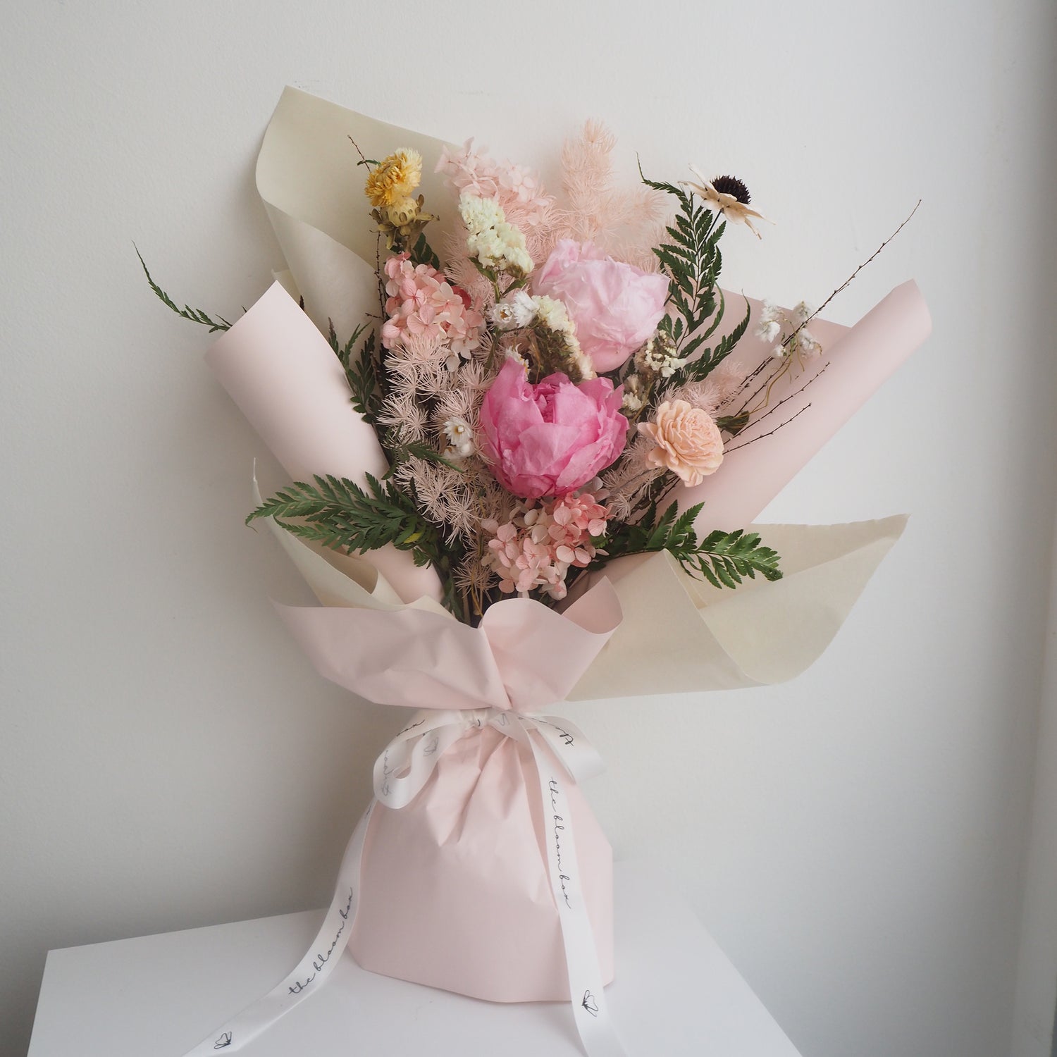 Bouquet of flowers wrapped in pink paper on a white surface with a light gray background