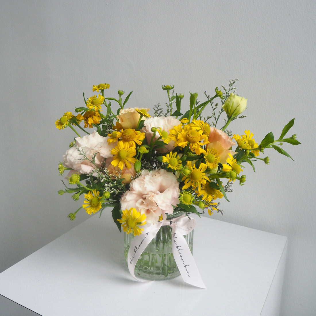 Bouquet of flowers in a clear vase on a white surface with a gray background