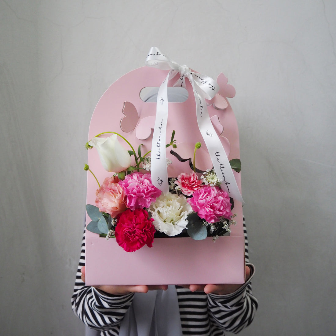 Pink gift box with flowers and a ribbon held by a person against a gray background