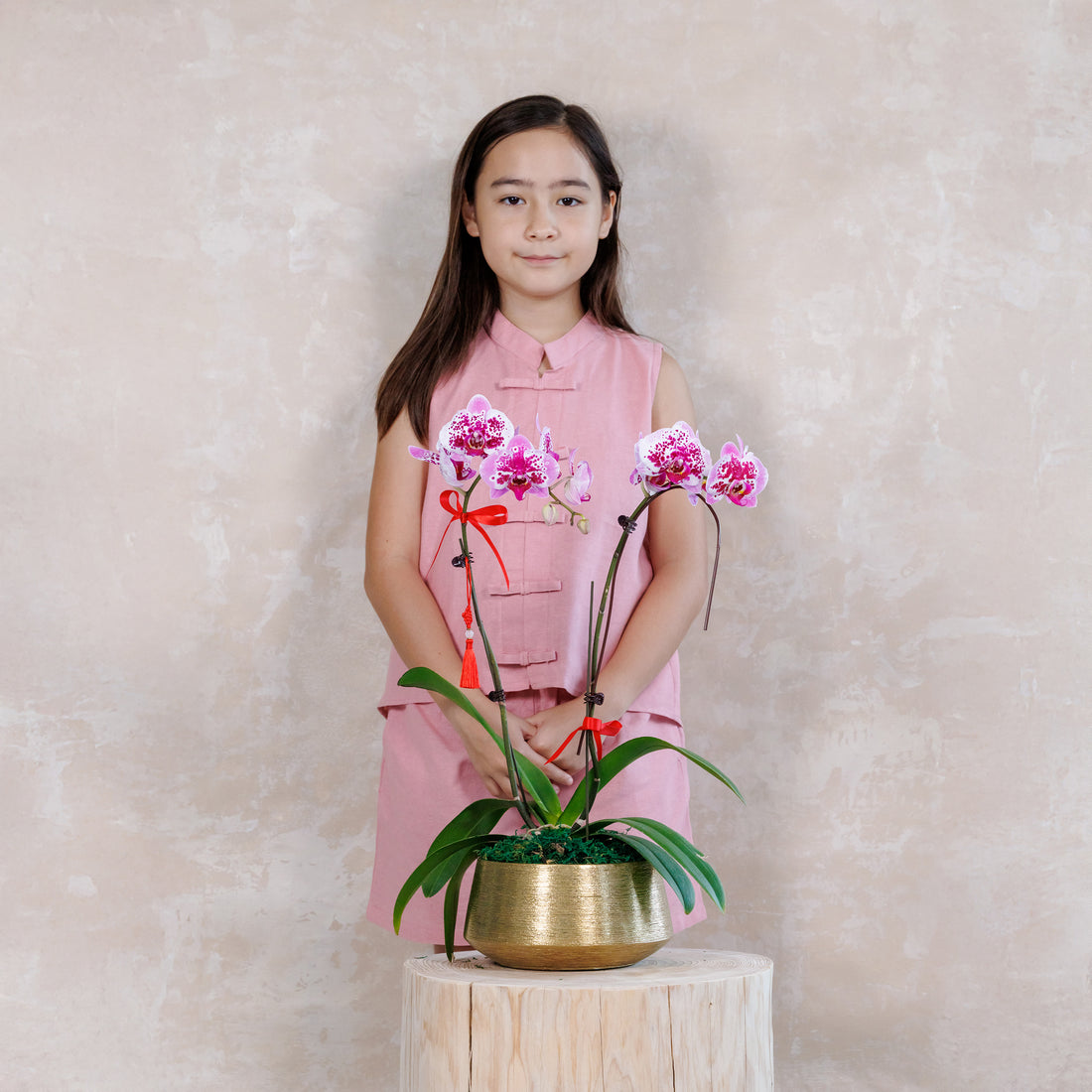 Young girl holding a potted orchid plant against a plain background