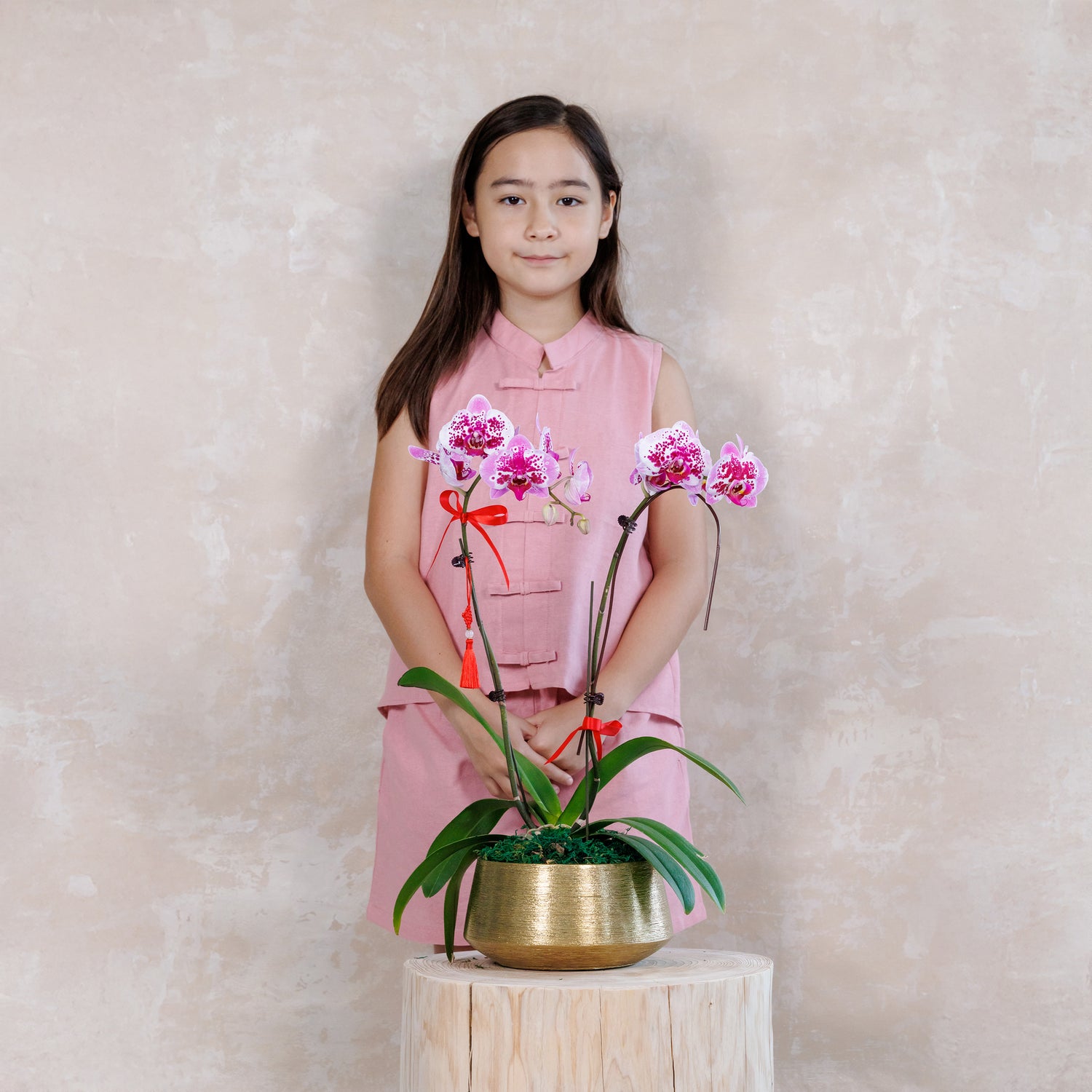 Young girl holding a potted orchid plant against a plain background