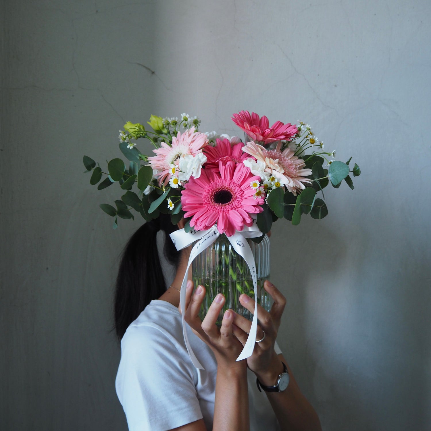 Person holding a bouquet of flowers in front of their face against a plain background