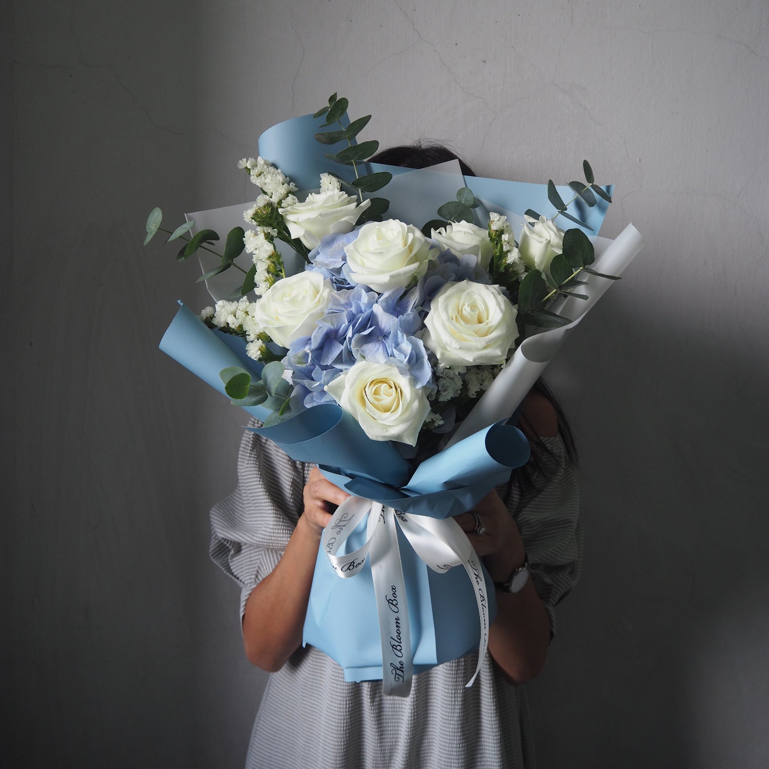 lady holding blue hydrangea and white roses with blue wrapper style bouquet