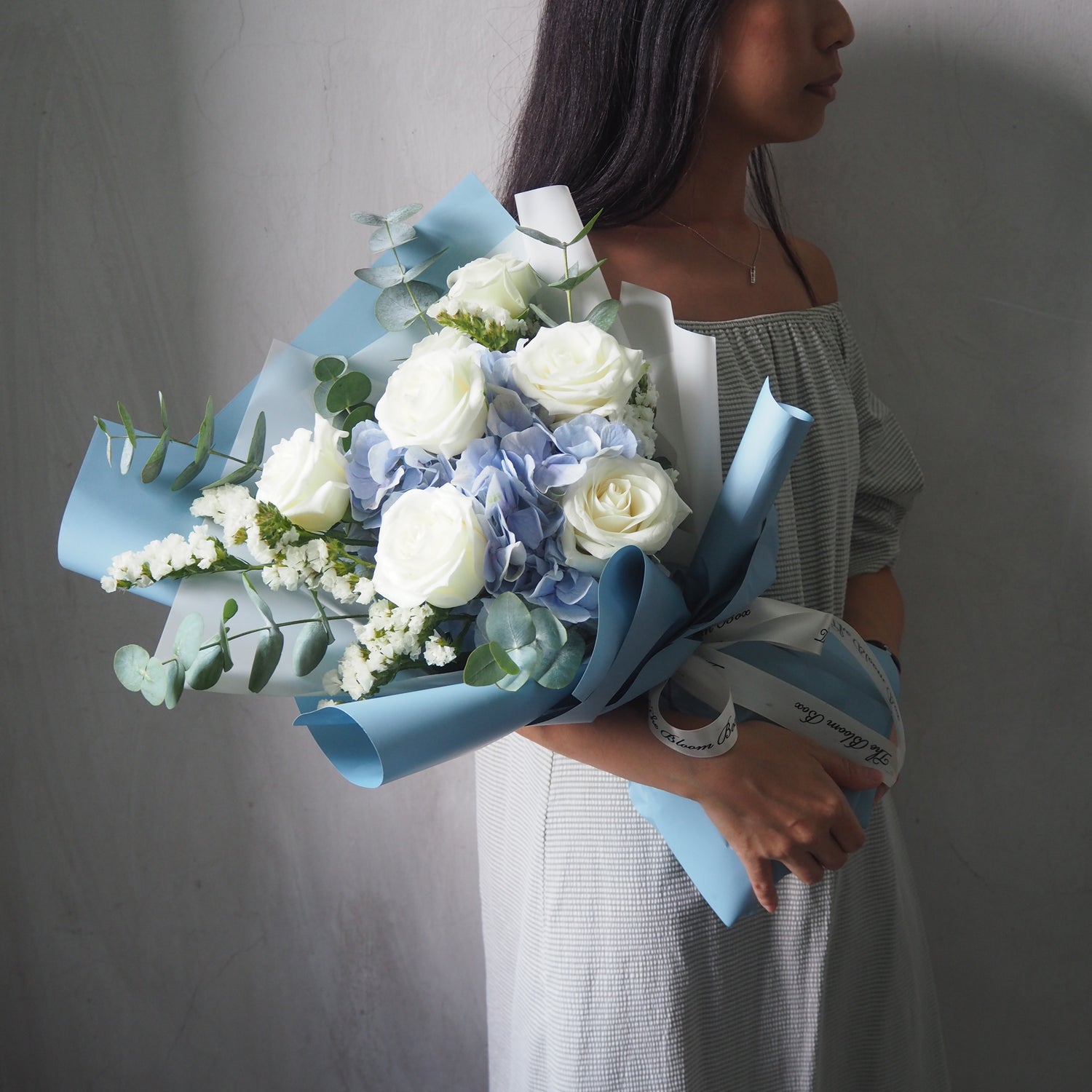 side view of lady holding blue hydrangea and white roses with blue wrapper style bouquet