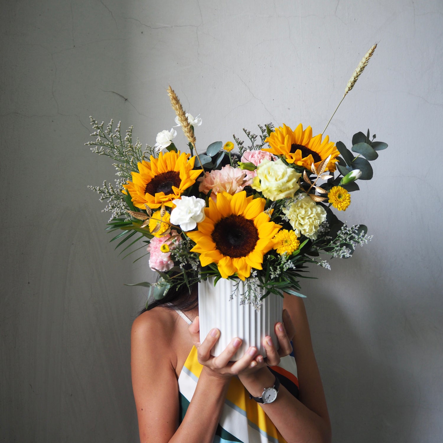 Person holding a bouquet of sunflowers and other flowers against a plain background