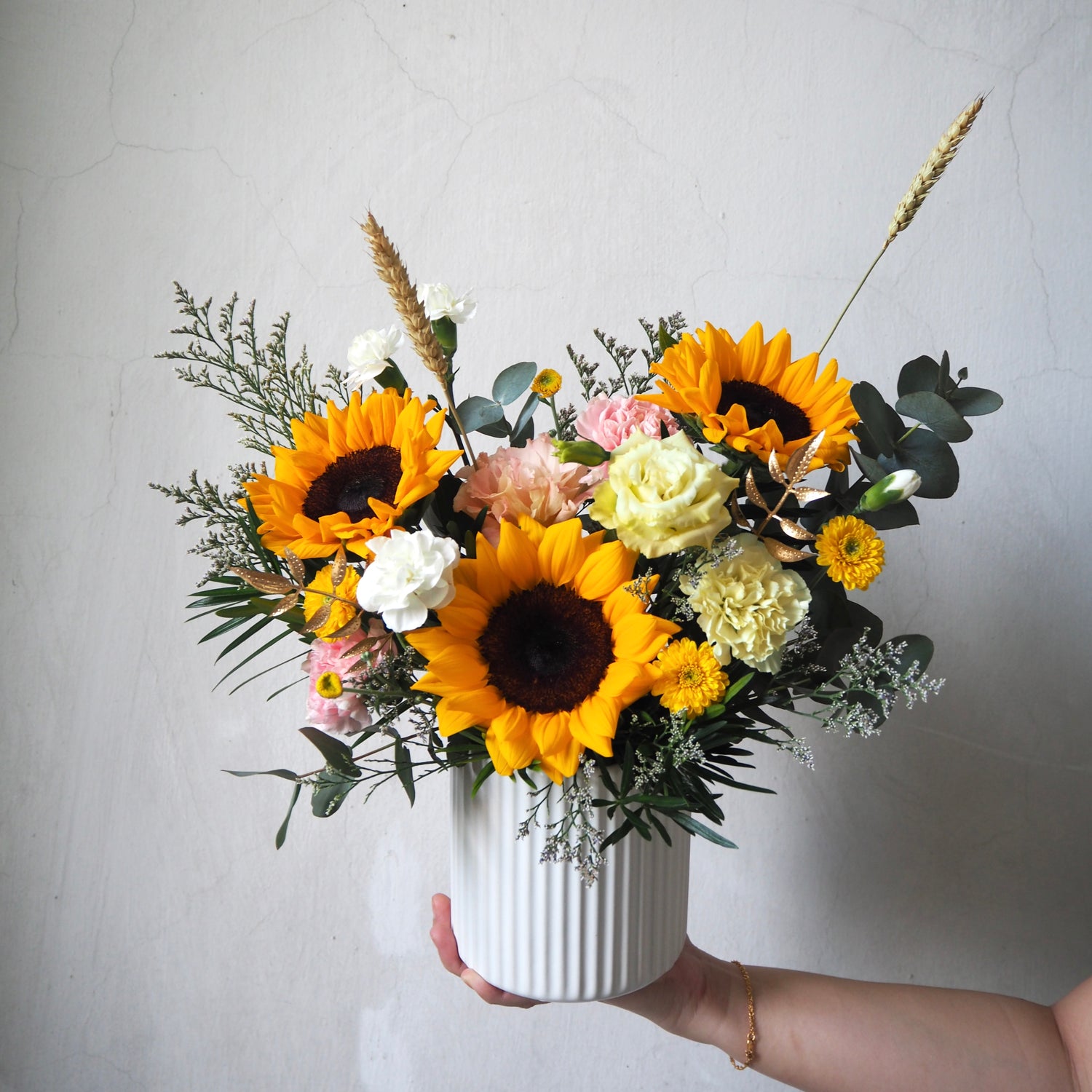 Bouquet of sunflowers and other flowers in a white vase against a plain background