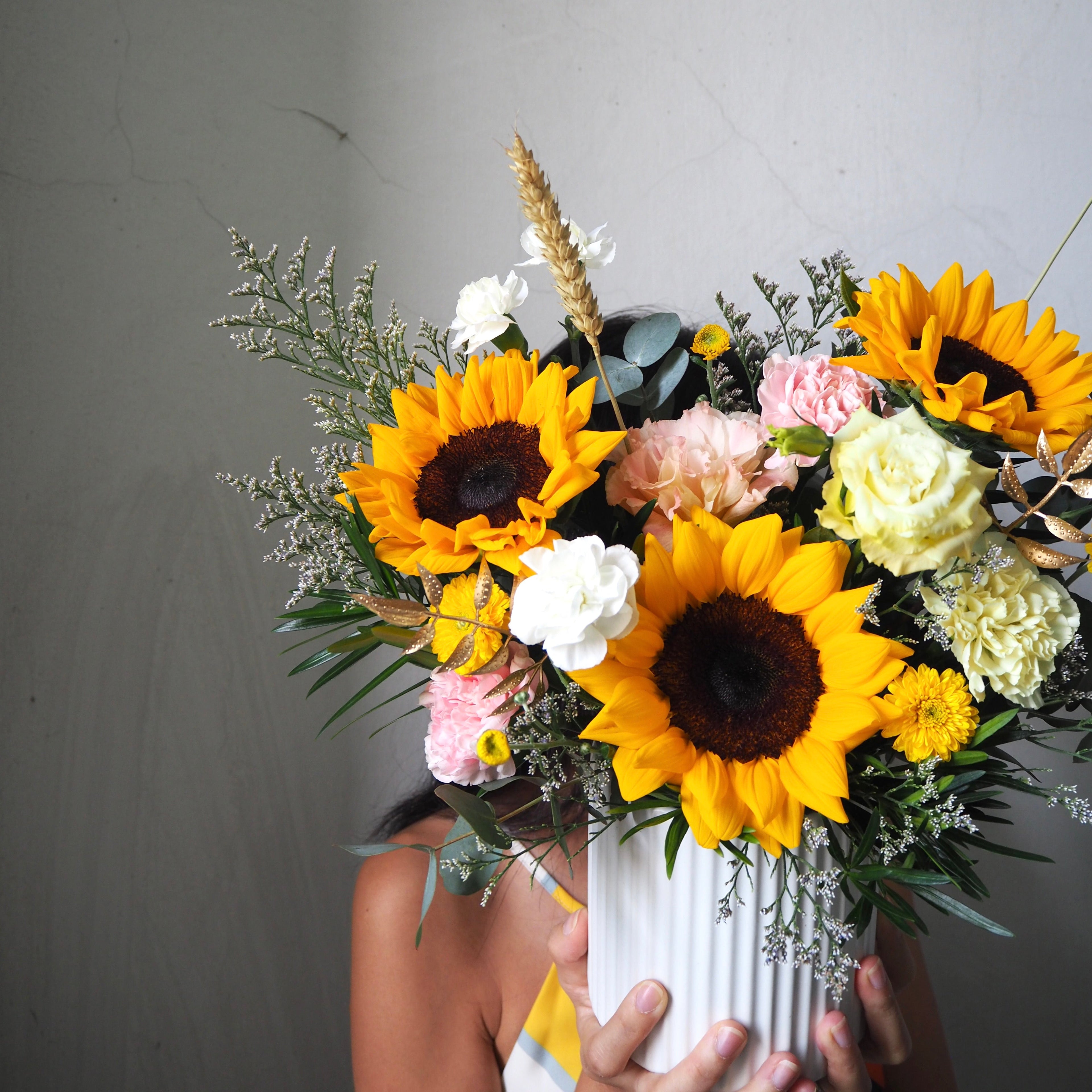 Bouquet of sunflowers and other flowers held against a gray background