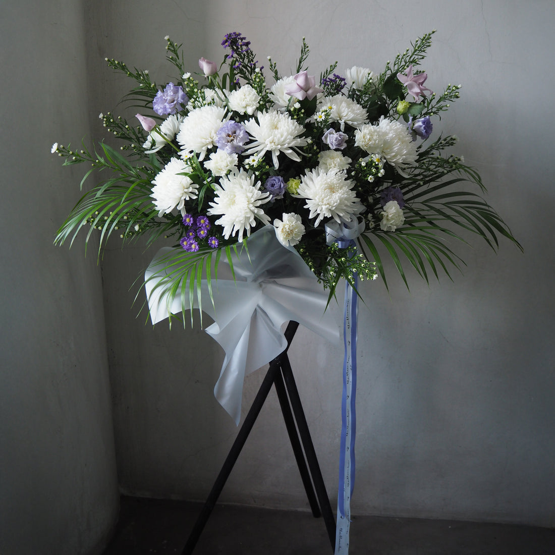 Bouquet of white and purple flowers with greenery on a stand against a plain background