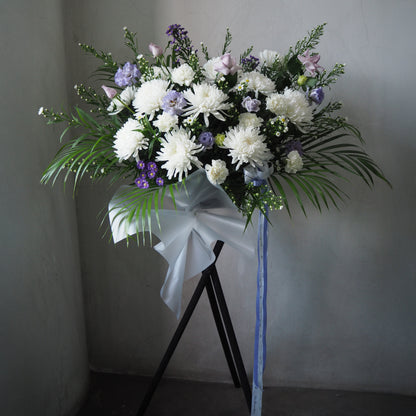 Bouquet of white and purple flowers with greenery on a stand against a plain background