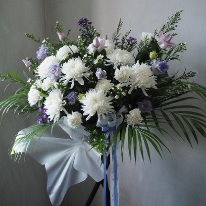 Bouquet of white and purple flowers with greenery on a stand against a plain background