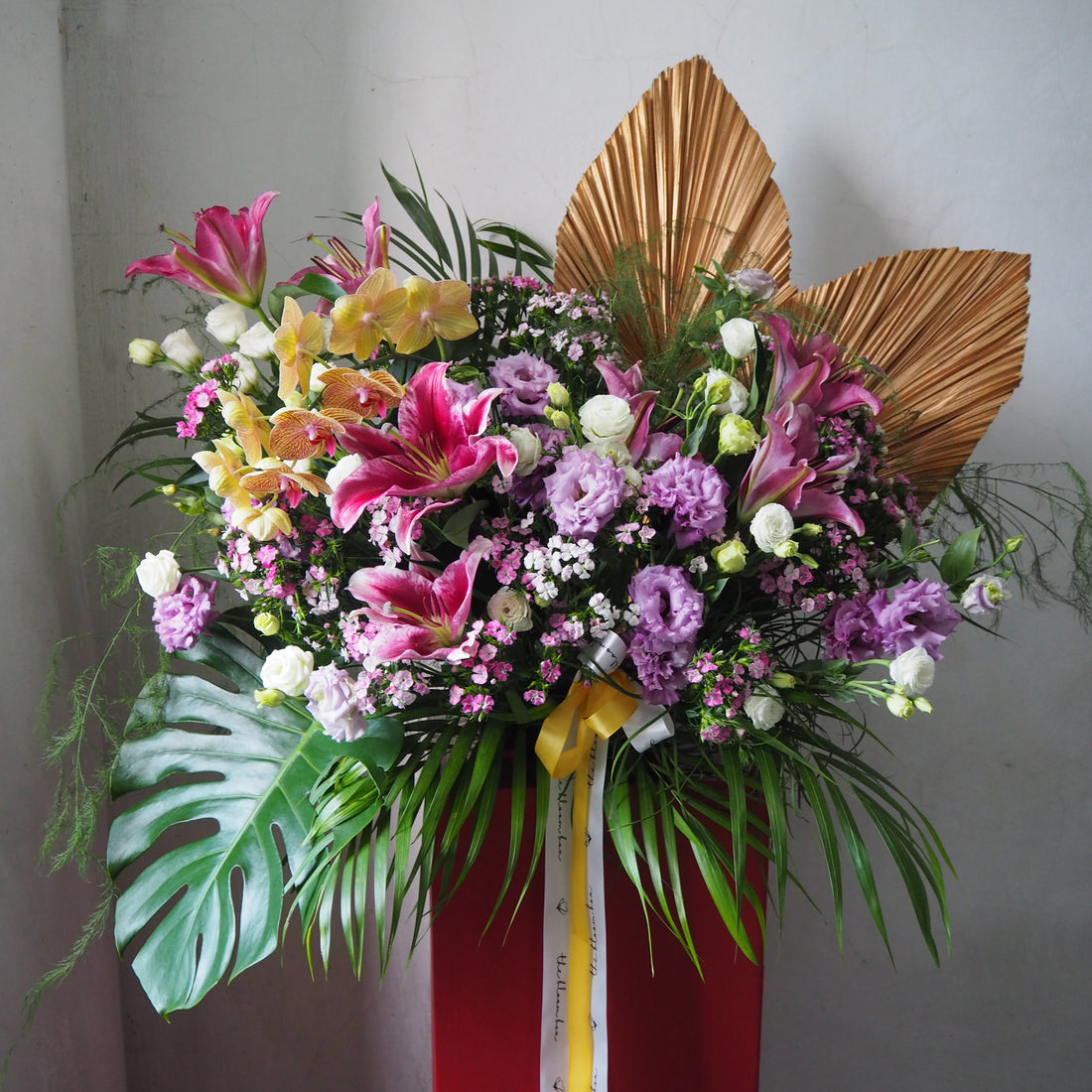 Colorful flower arrangement with a red base and gold leaves on a plain background