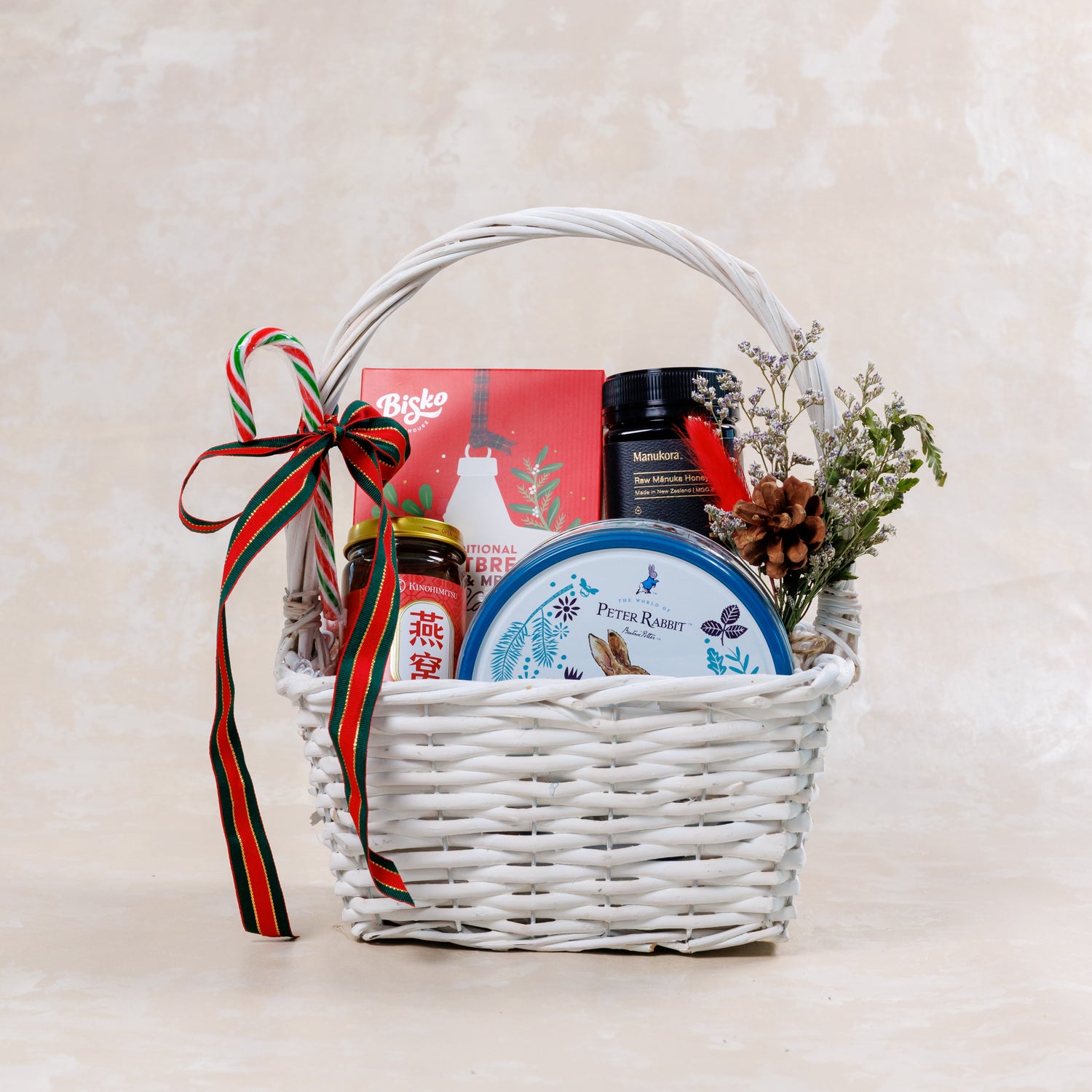 Gift basket with various items including a jar, a box, and a container, tied with a ribbon on a light background.