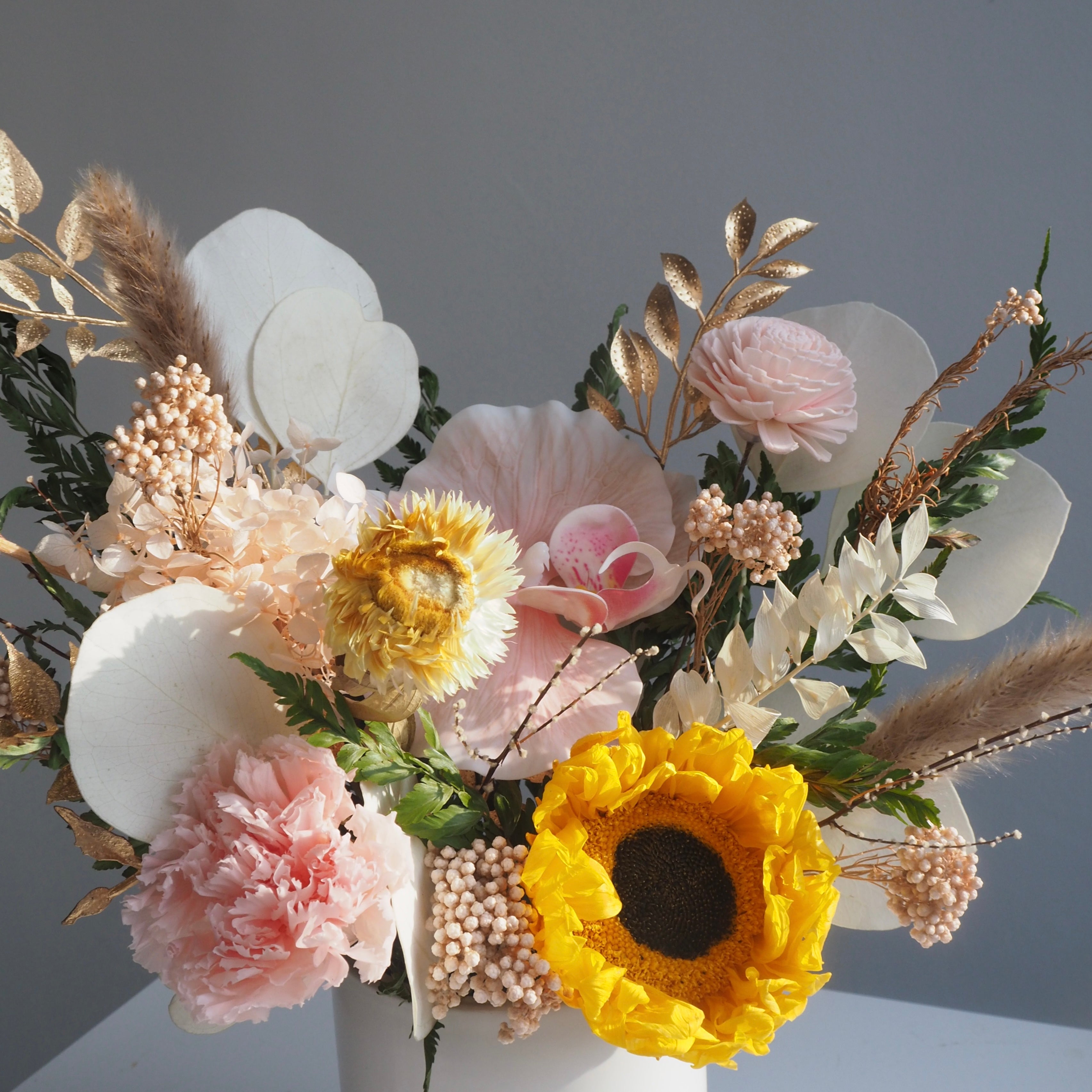 Close-up of preserved yellow sunflowers in Saffron vase, showing vibrant color retention and soft peach tones