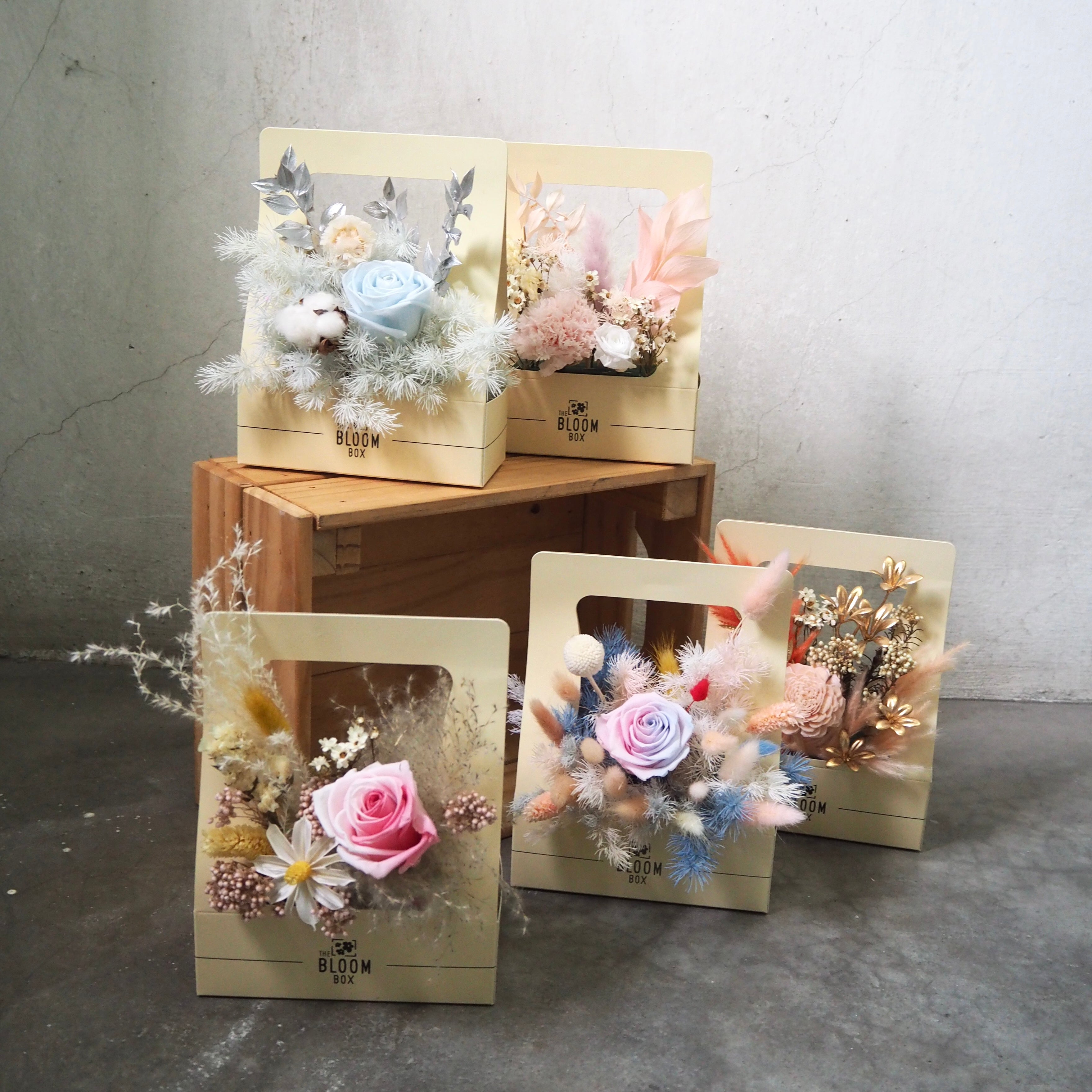 Decorative flower arrangements in wooden boxes on a concrete floor.