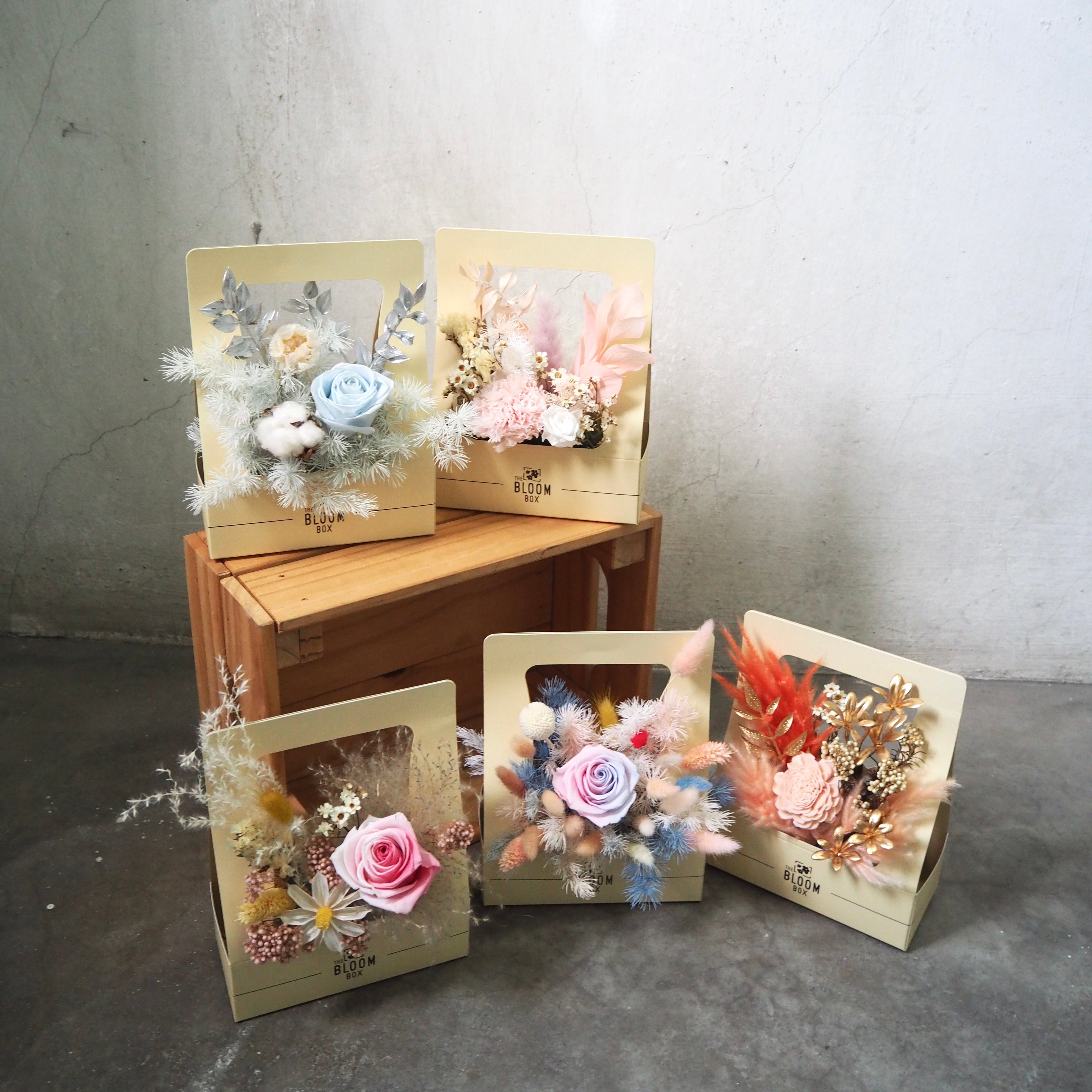 Decorative boxes with floral arrangements on a wooden surface and concrete floor.