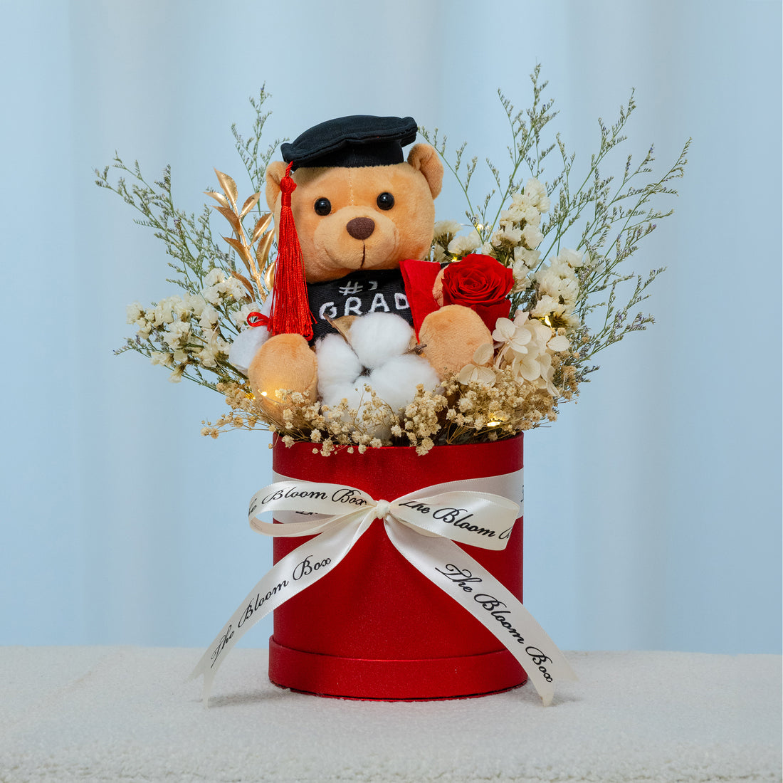 graduation bear sitting in red box with preserved red rose arrangement